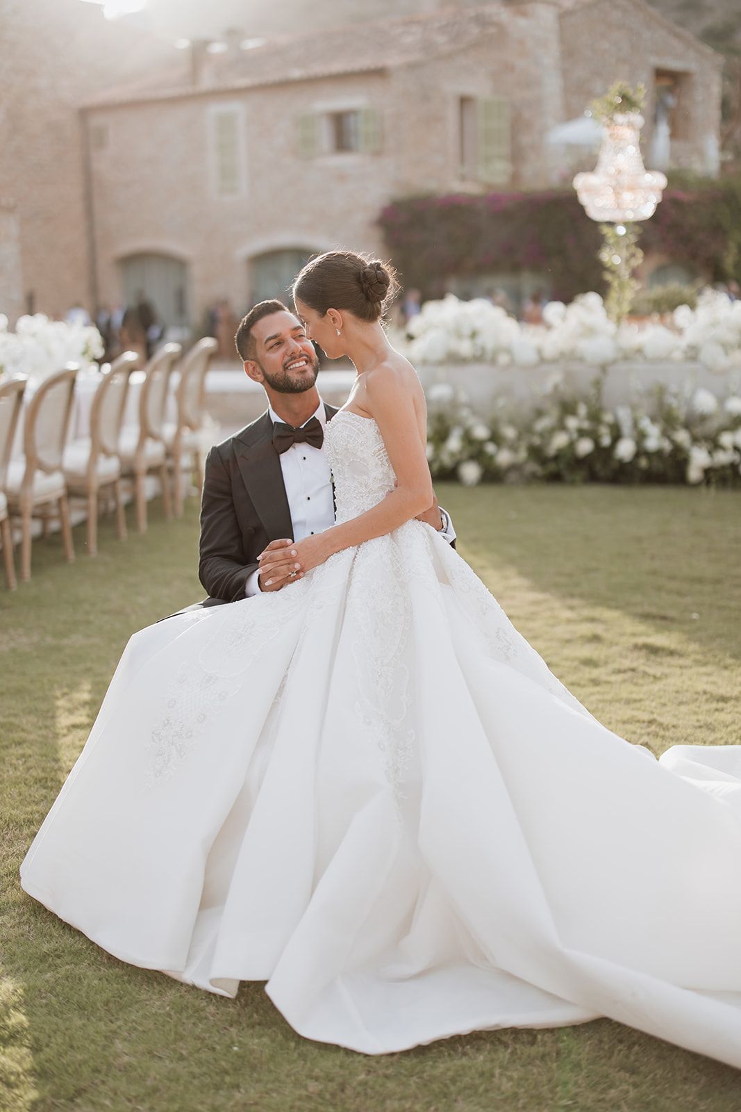 Newlyweds share romantic moments on a sunlit lawn with a flowing white wedding gown.