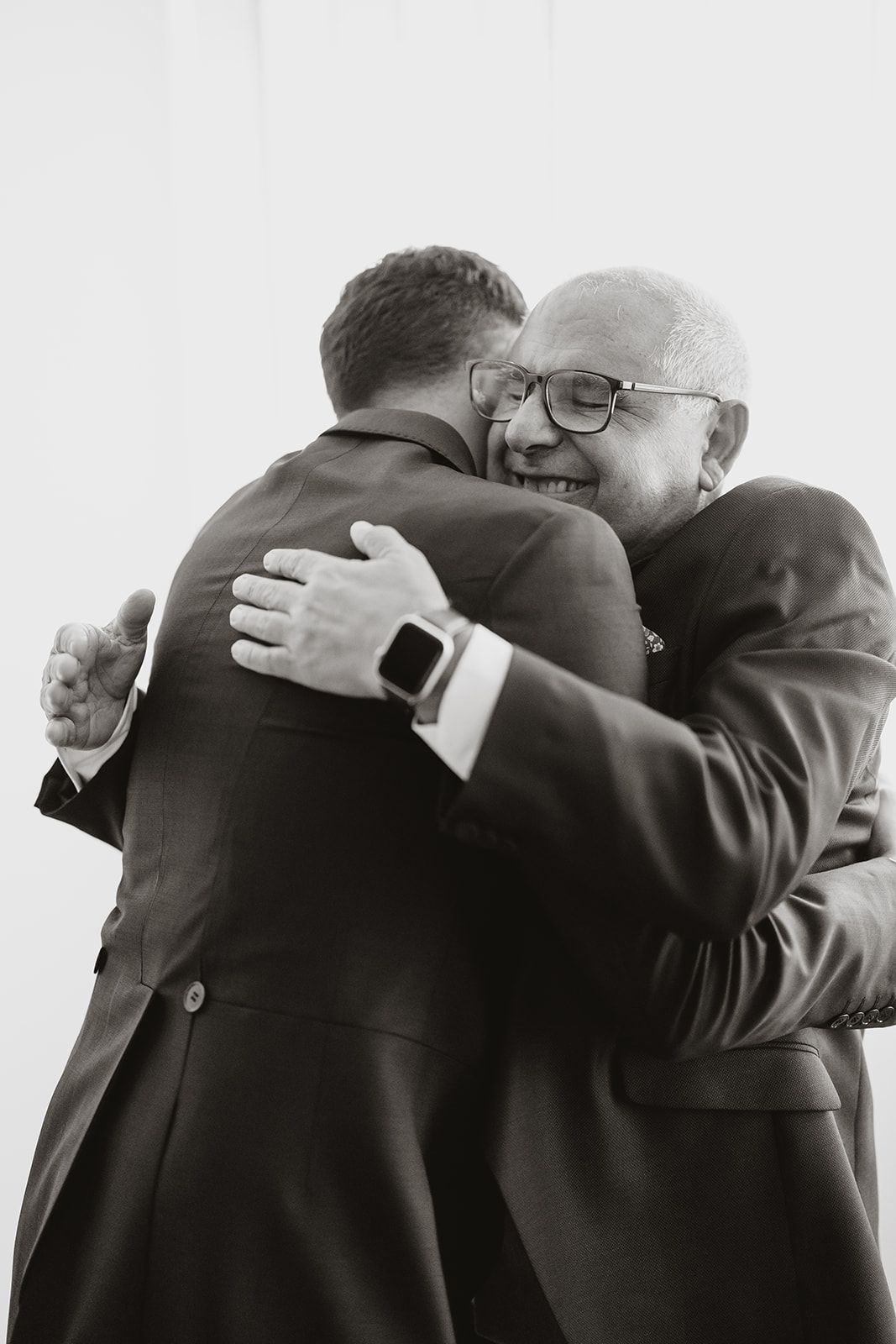 Two people share a warm embrace in formal attire captured in black and white.