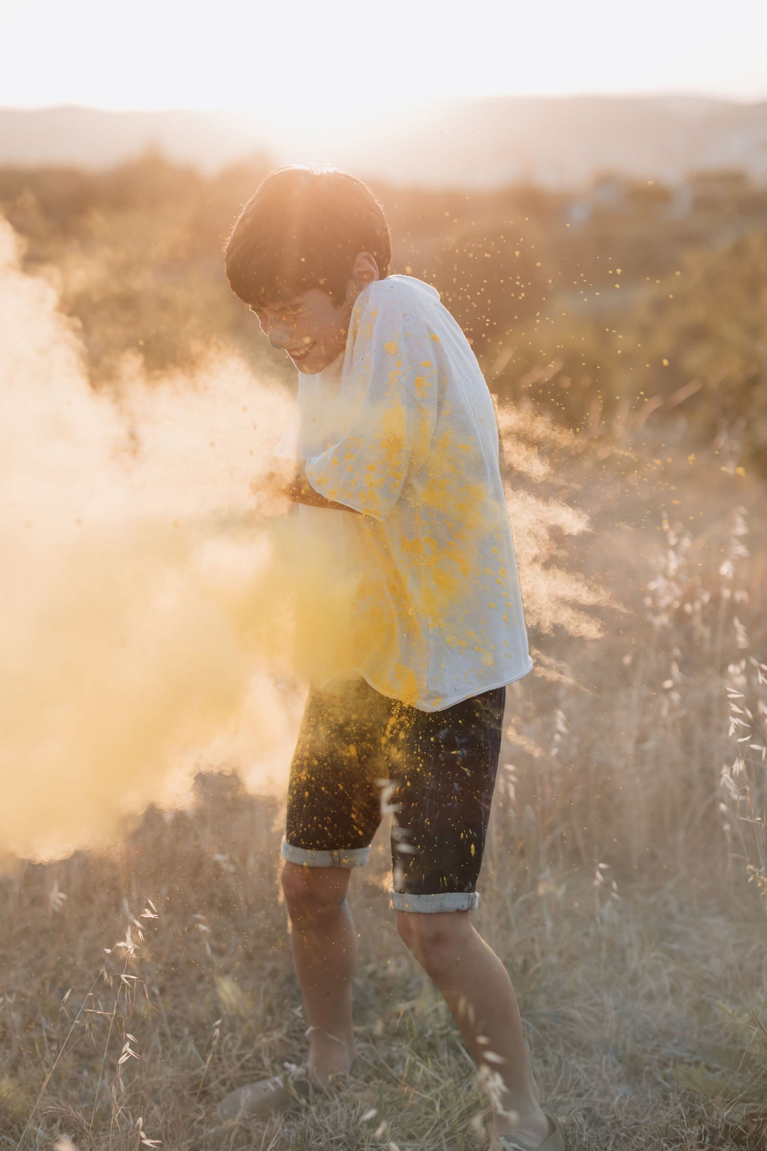 Person in yellow shirt stands in a misty golden field at sunset, surrounded by ethereal dust particles in backlight.