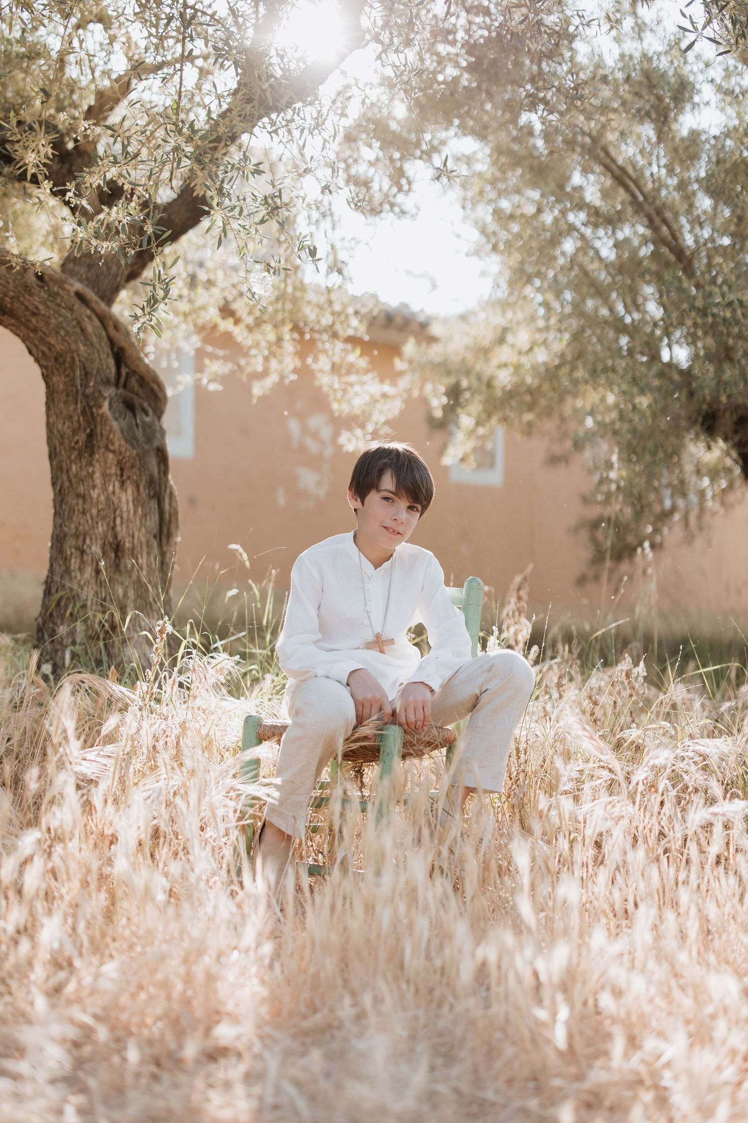 A person wearing all white sits in a dreamy sunlit meadow with tall golden grass beneath a large tree.