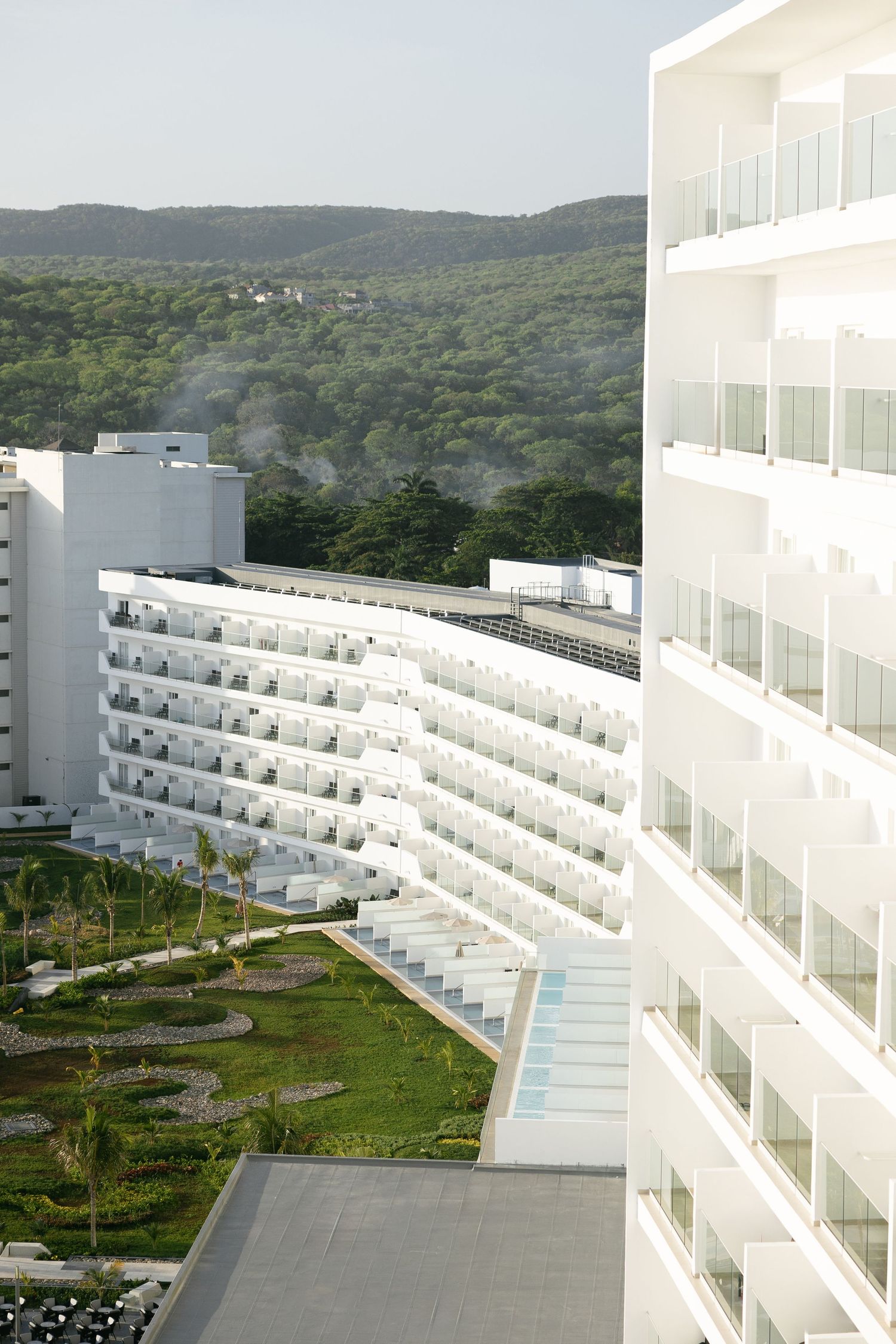 Luxury hotel complex with tiered balconies set against tropical forest backdrop.