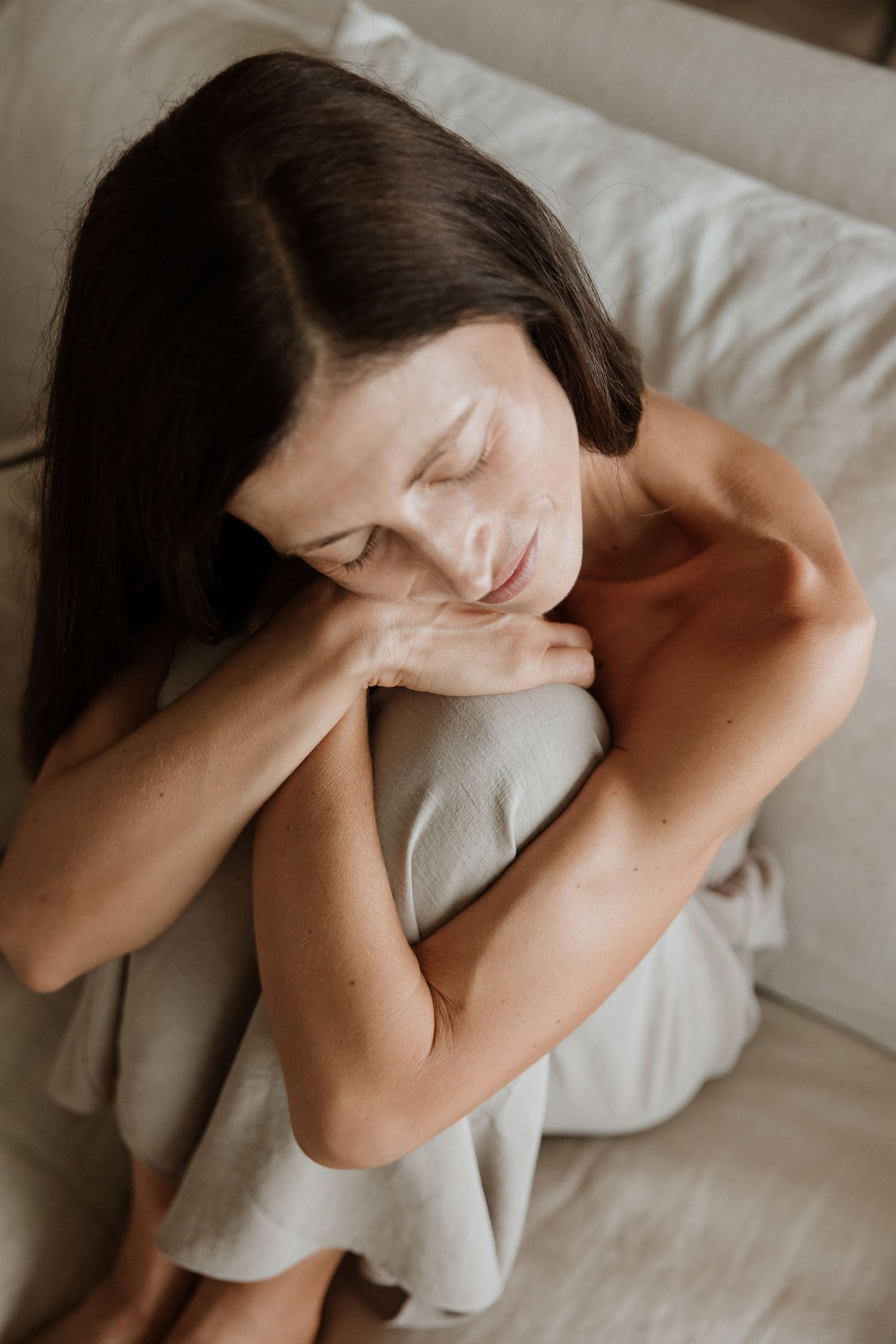 Soft moody portrait of person in contemplative pose on white couch.