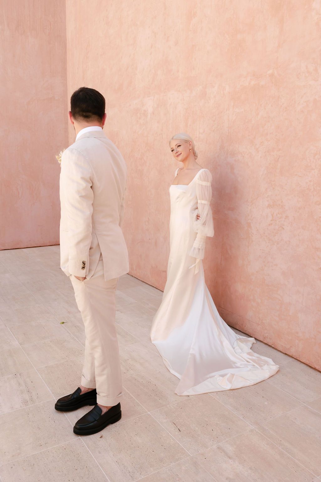 Minimalist wedding portrait with couple in white and cream against blush colored wall.