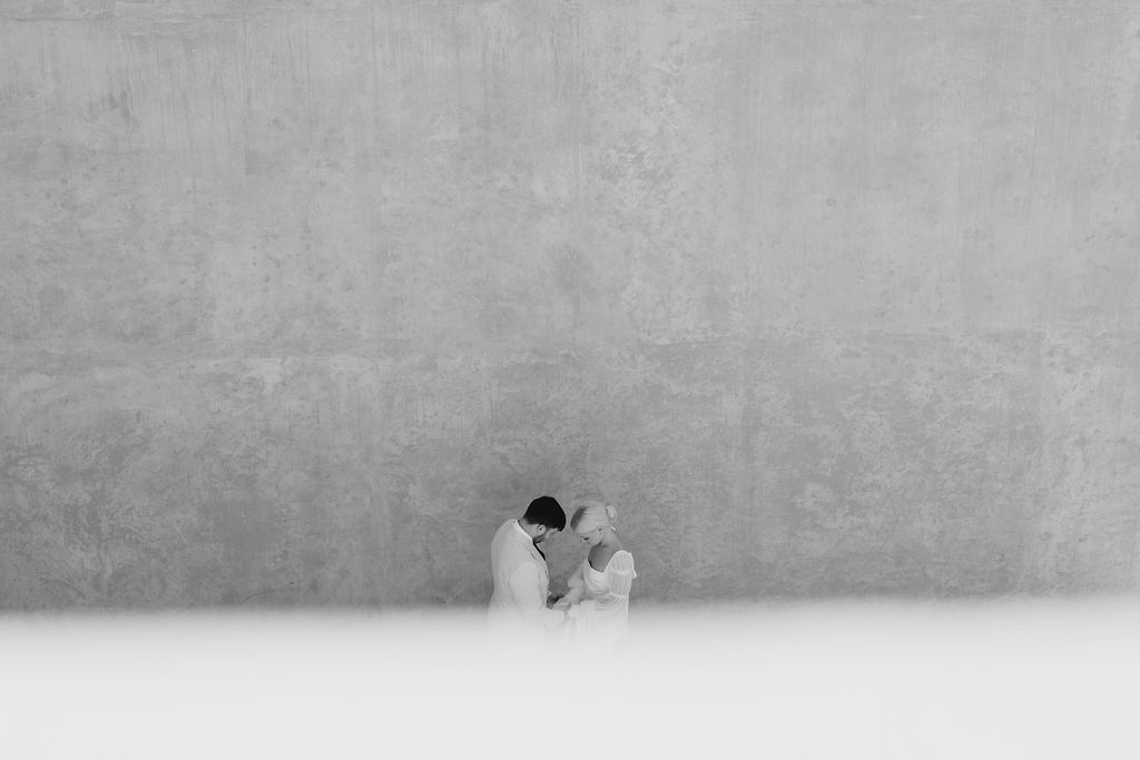Minimalist black and white wedding portrait against stark concrete wall.
