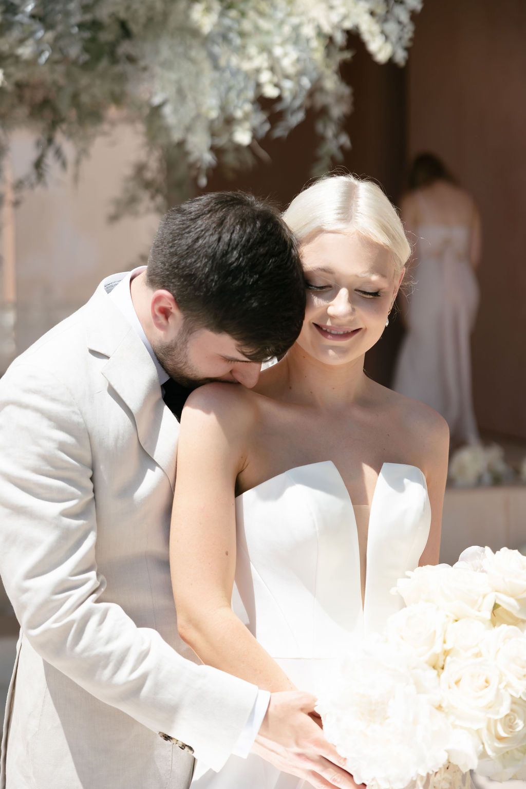 A tender wedding moment captured under decorative white flowers.