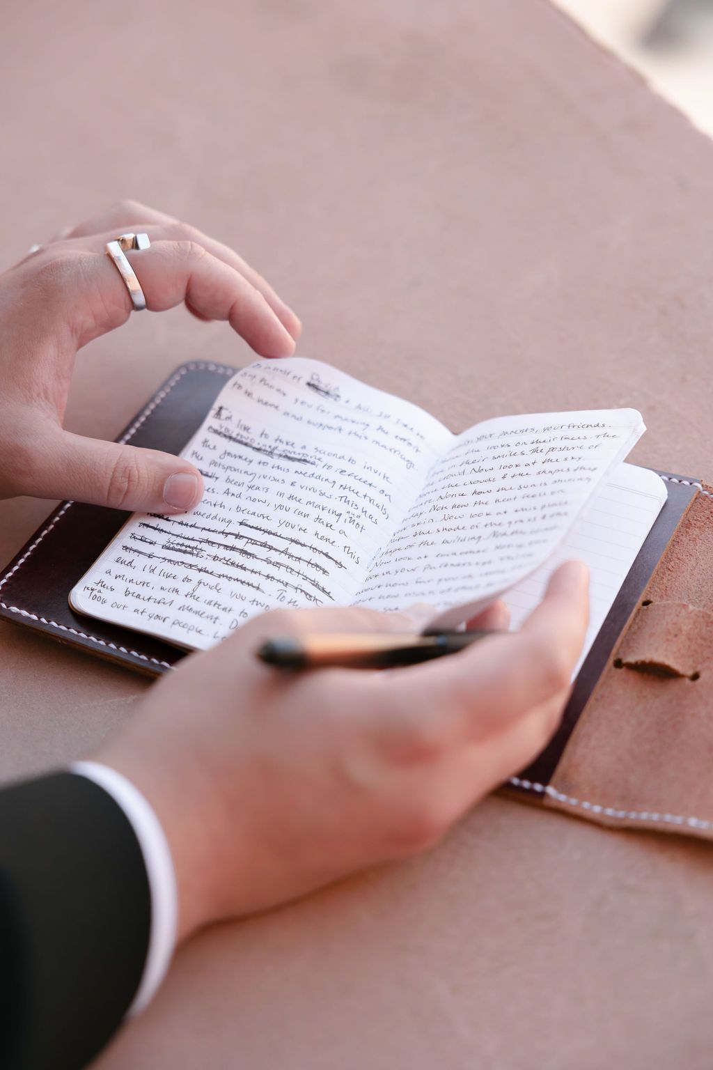 Hands holding an open leather-bound book with handwritten text.