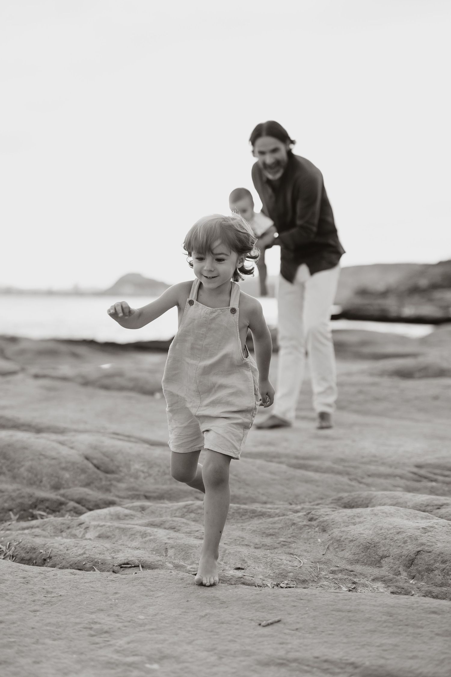 Child plays energetically on rocky coastal terrain in black and white.