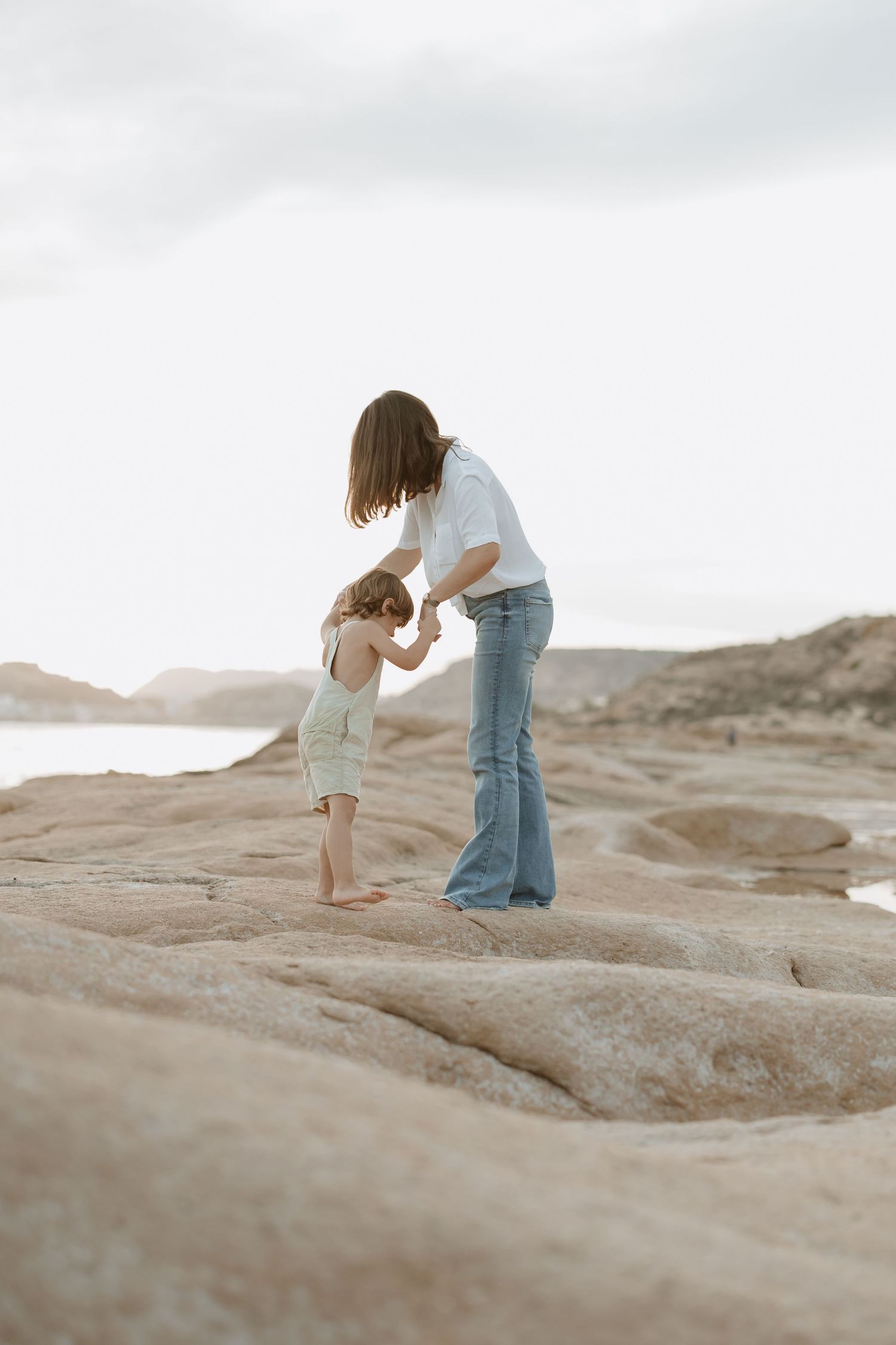 Mother and child share special moment while climbing on coastal rocks.