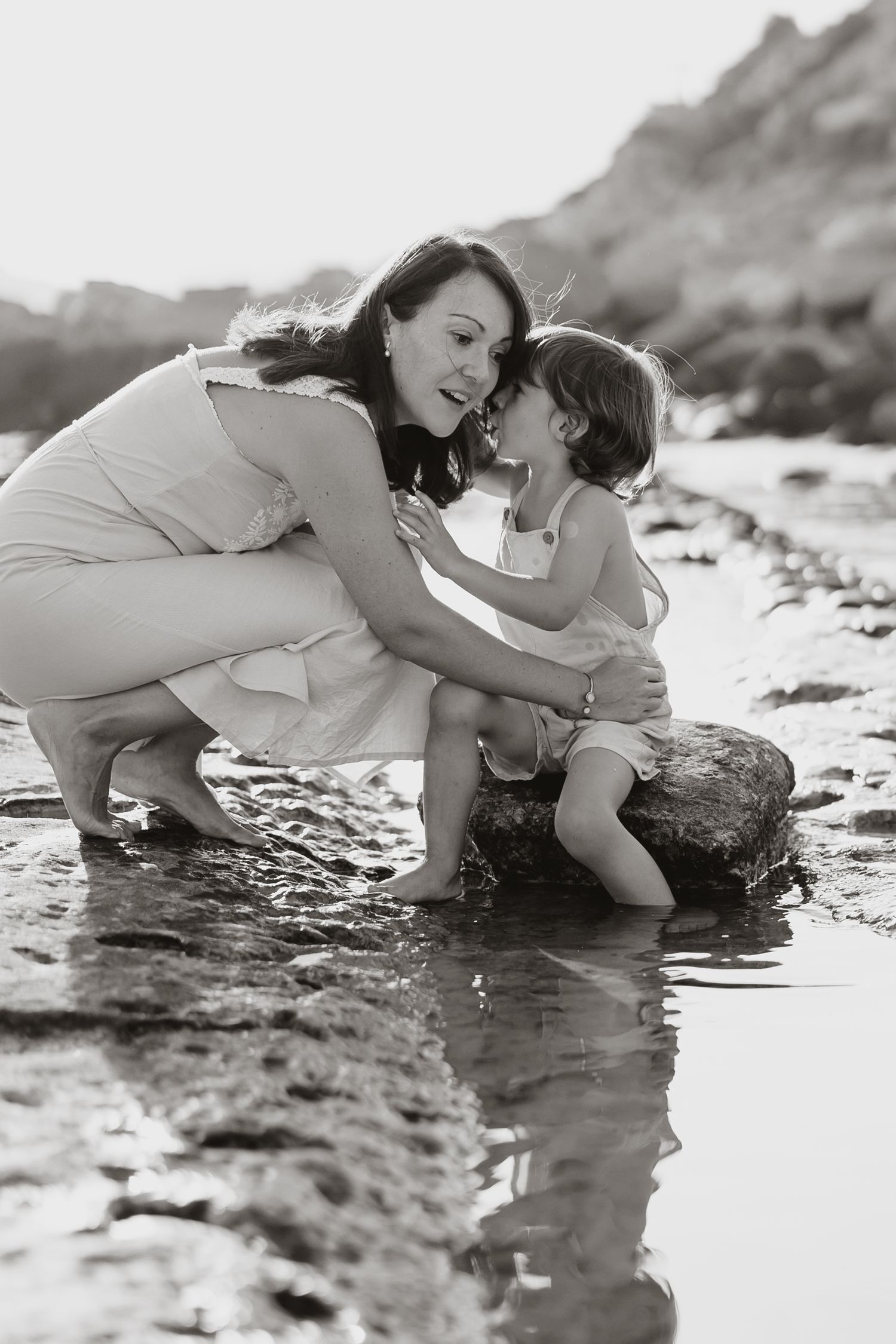 Two people share tender moment while exploring rocky beach at sunset.