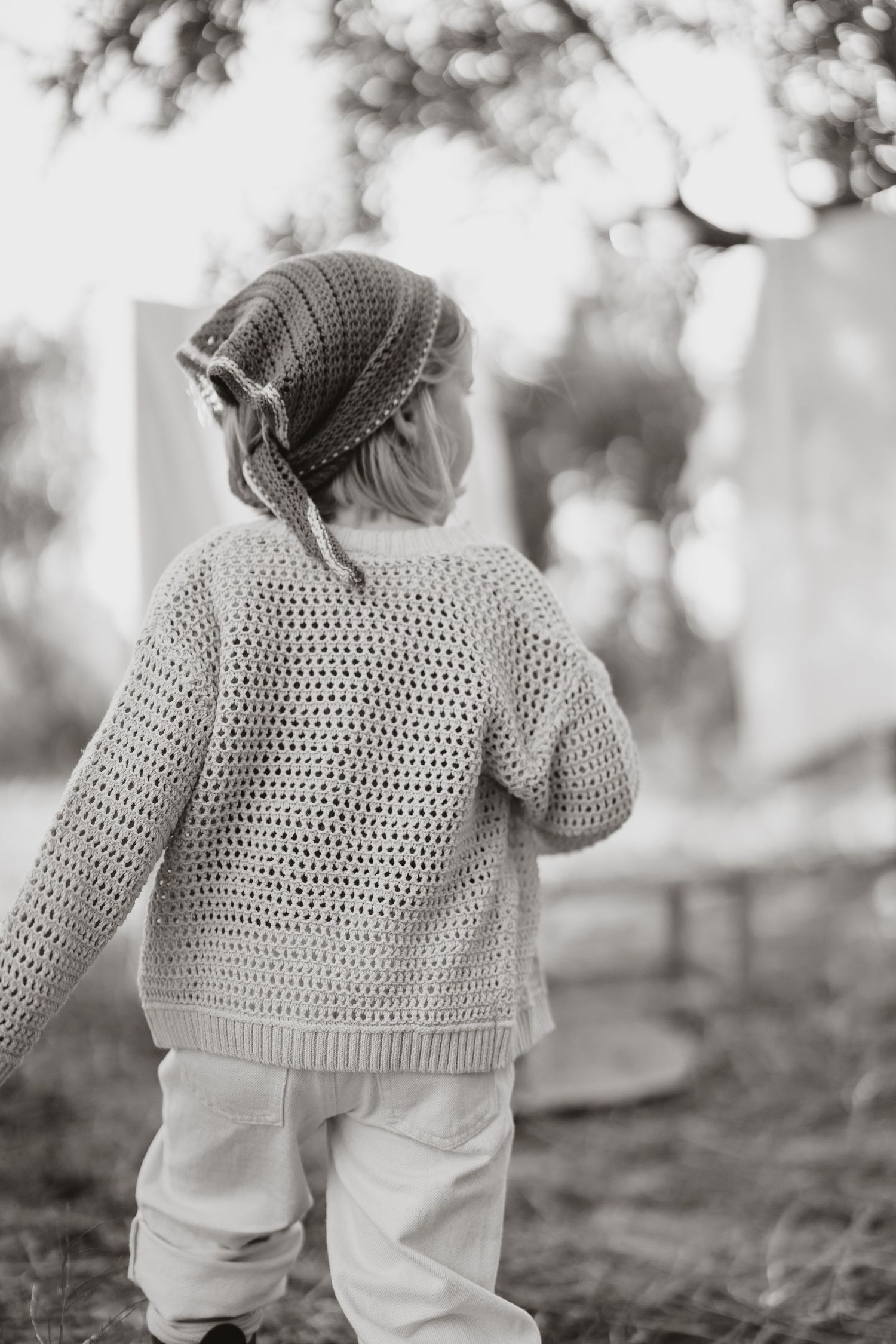 Back view of small figure wearing crochet sweater and white pants walking outdoors.