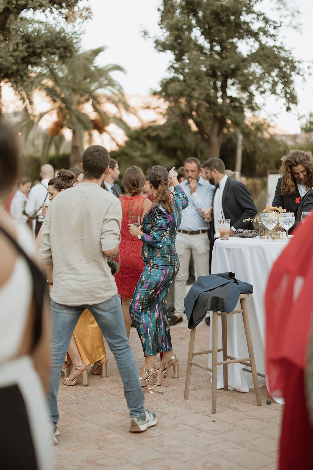 Wedding guests mingle at an outdoor cocktail reception with palm trees in the background.