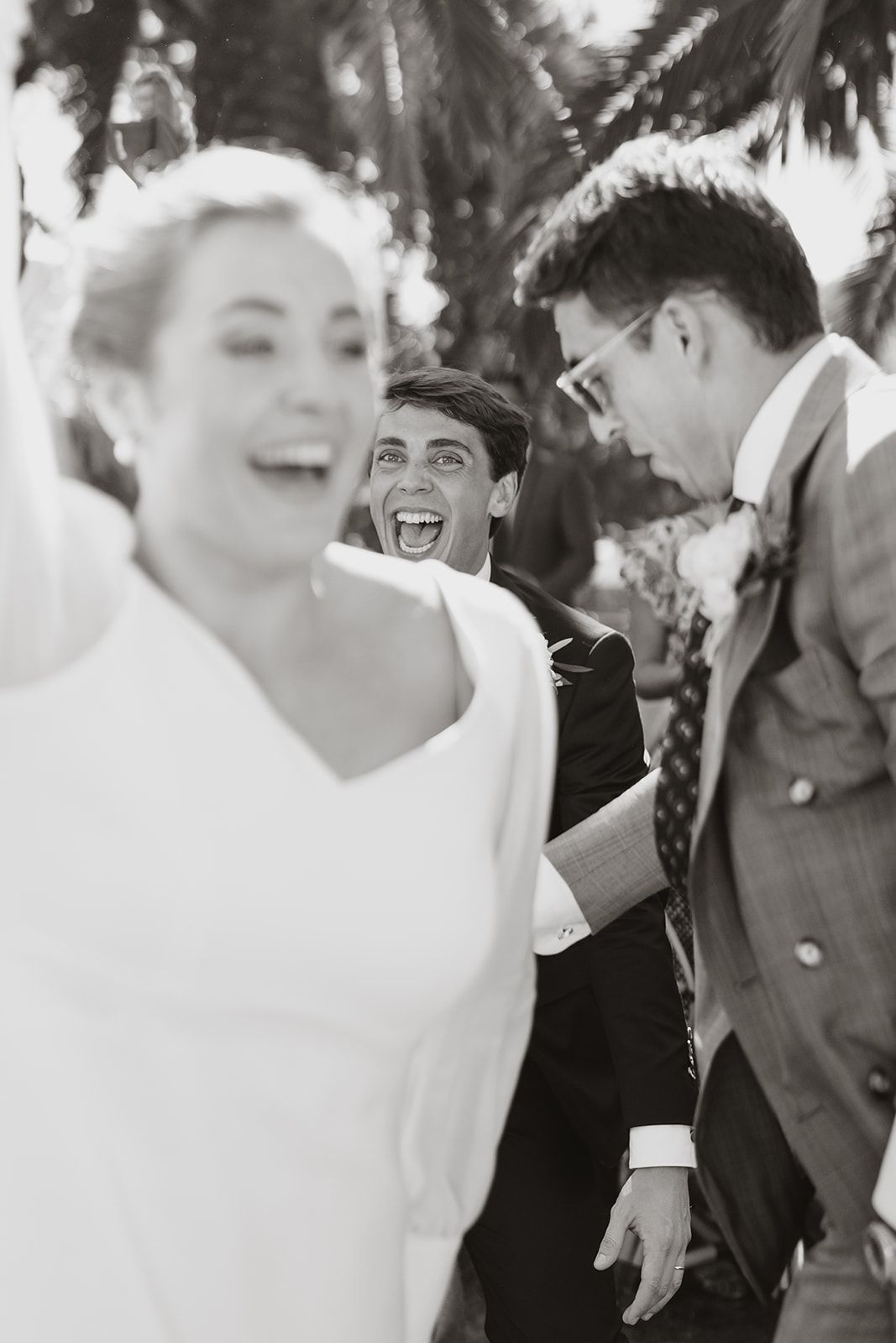 Candid black and white wedding photo capturing laughter and joy during outdoor celebration.