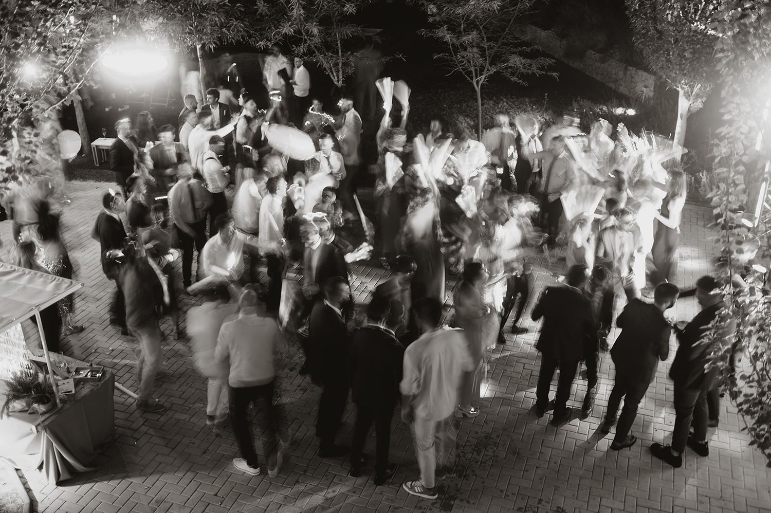 Black and white shot of wedding guests mingling and dancing at an outdoor reception.