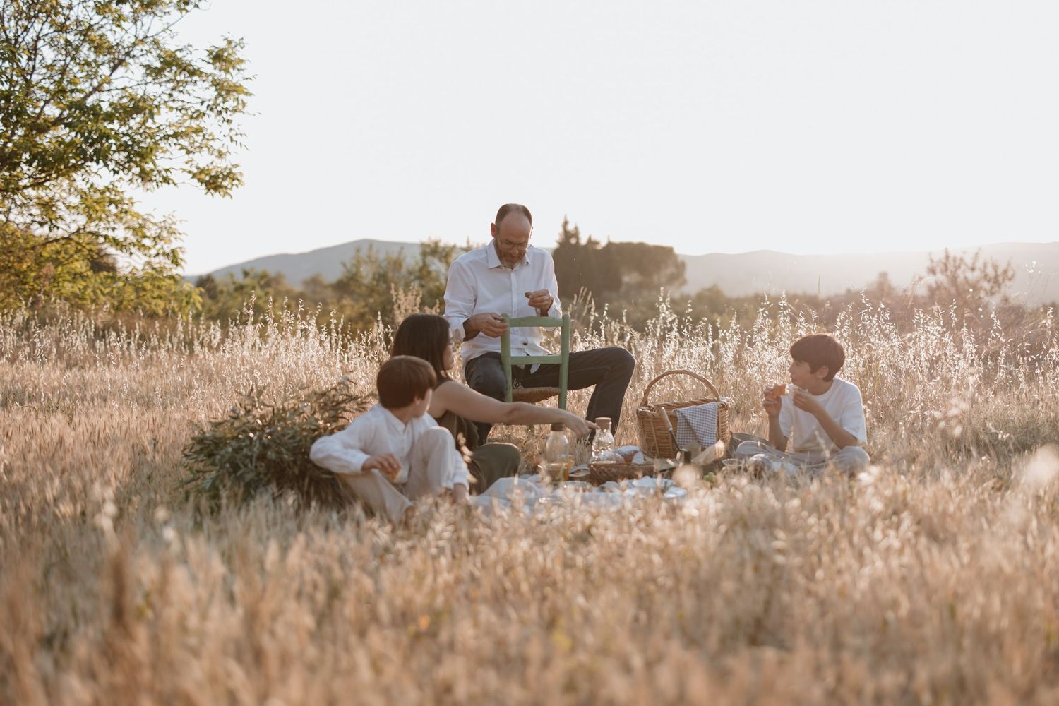 People having a picnic together in a golden field during sunset with mountains in the background.