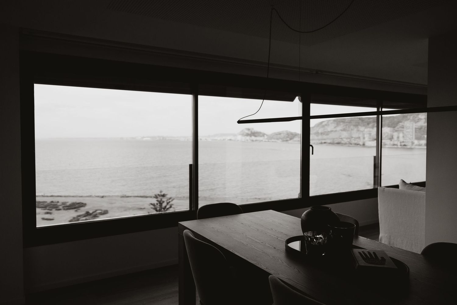 Panoramic view through large windows showcasing coastal landscape and ocean.