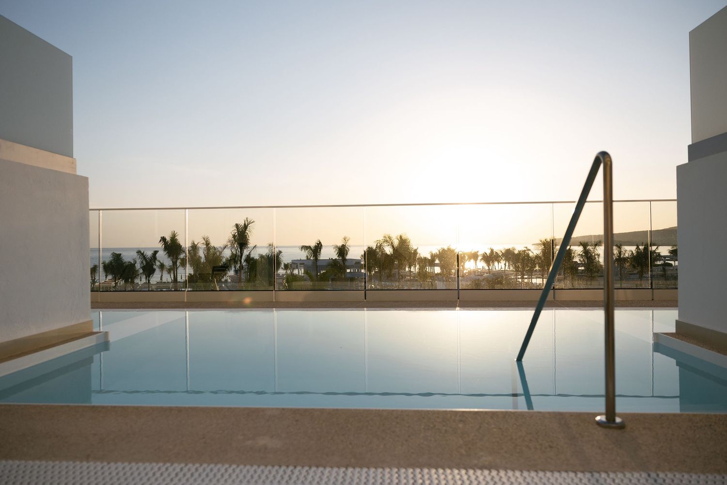 Modern pool terrace with ocean view and safety railings during golden hour.