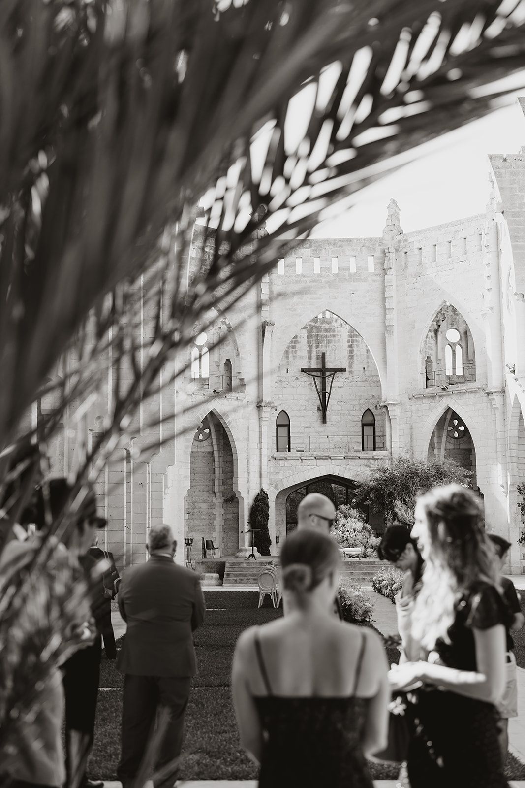 Black and white photo of wedding ceremony setup viewed through palm fronds at historic church venue.
