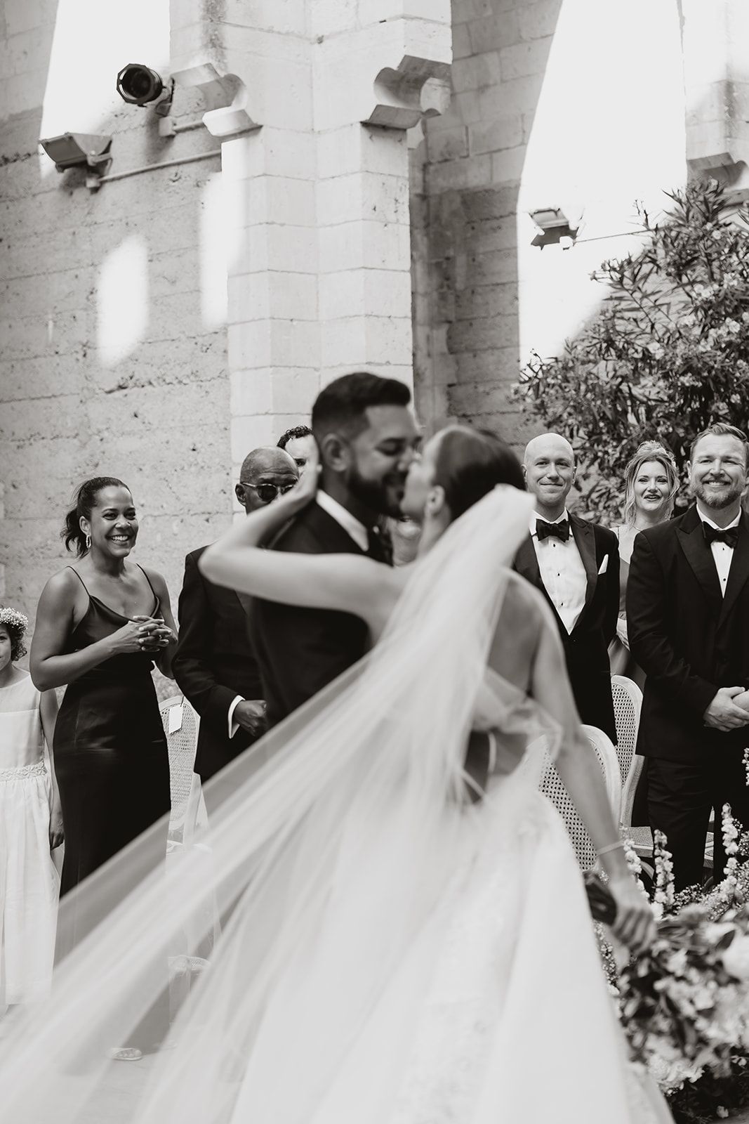 Black and white wedding ceremony photo with guests watching in a stone courtyard.