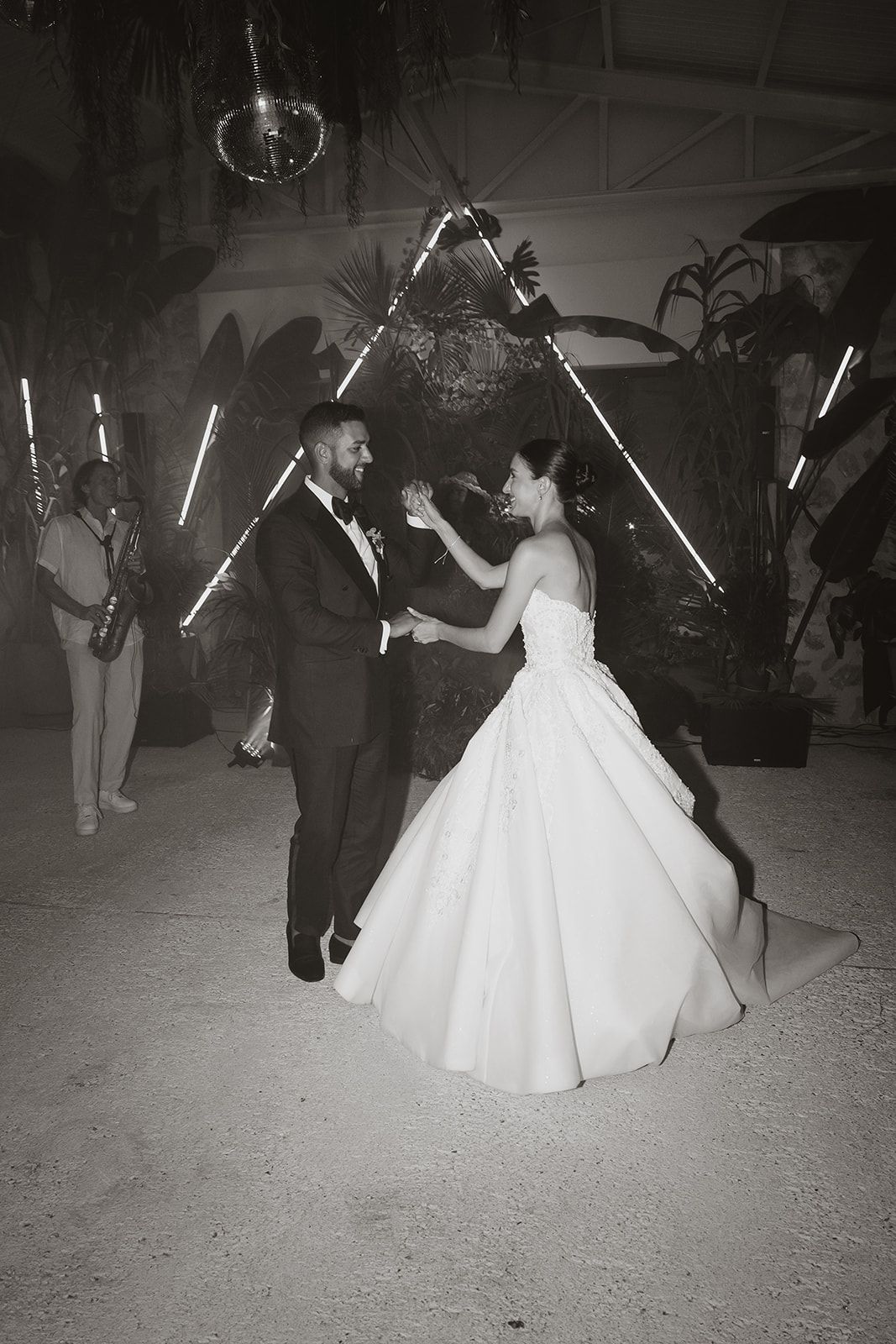 Black and white photo of newlyweds dancing under geometric light installation.
