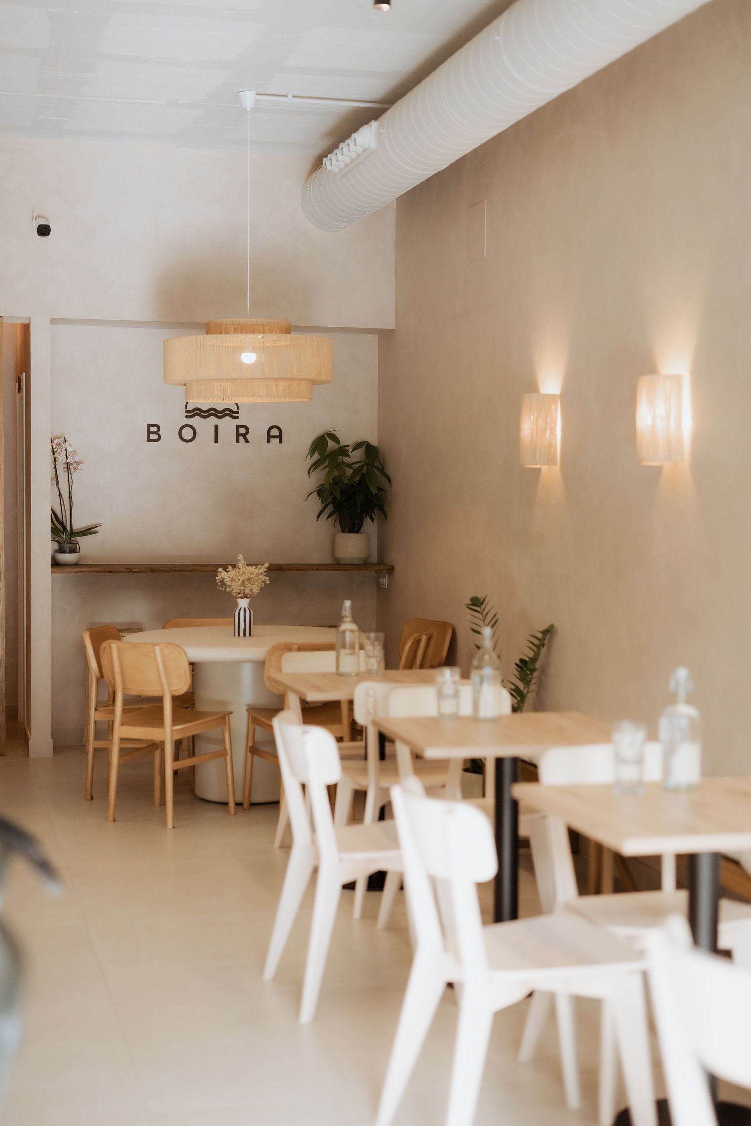 Minimalist Boira restaurant interior with light wood chairs, beige walls, woven pendant light, and soft wall sconces.