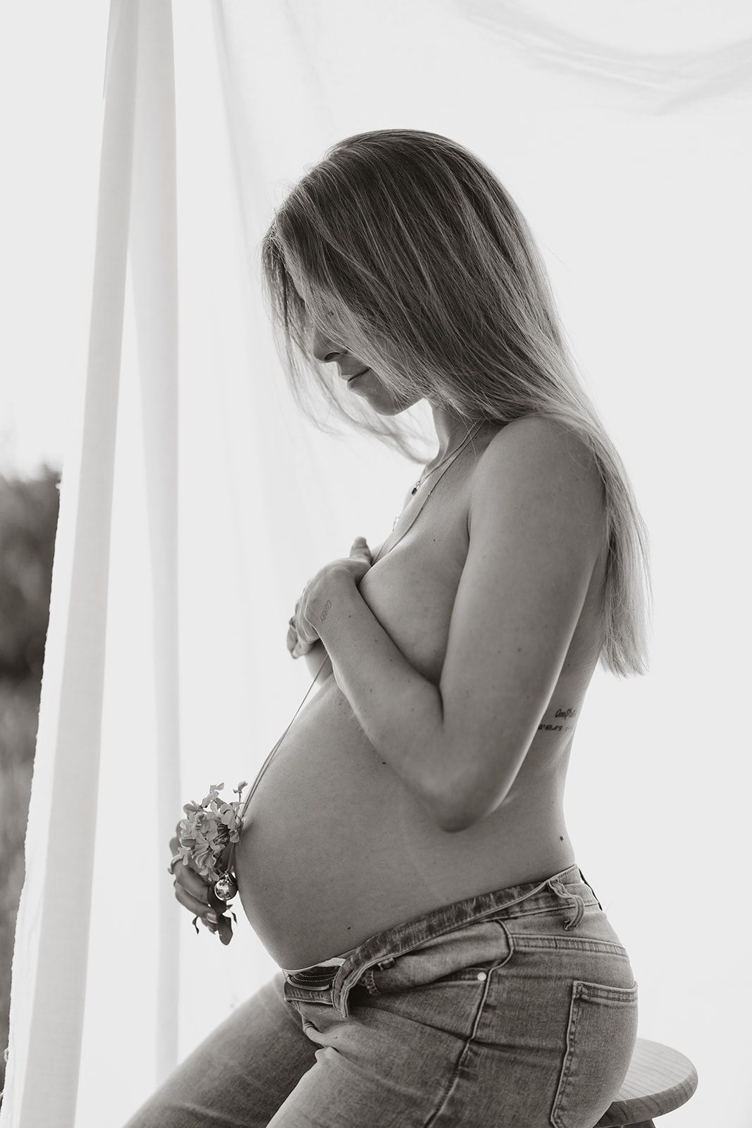 Artistic black and white maternity photo highlighting pregnant silhouette against white backdrop.