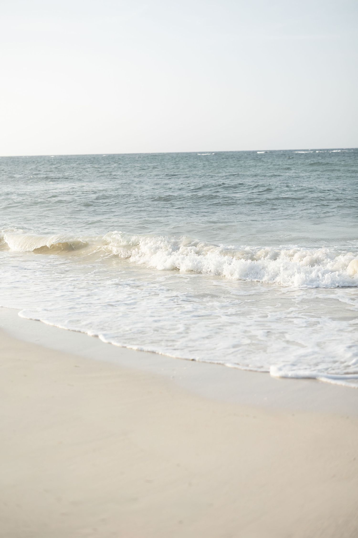 Serene beach scene with gentle waves rolling onto sandy shore under soft lighting.