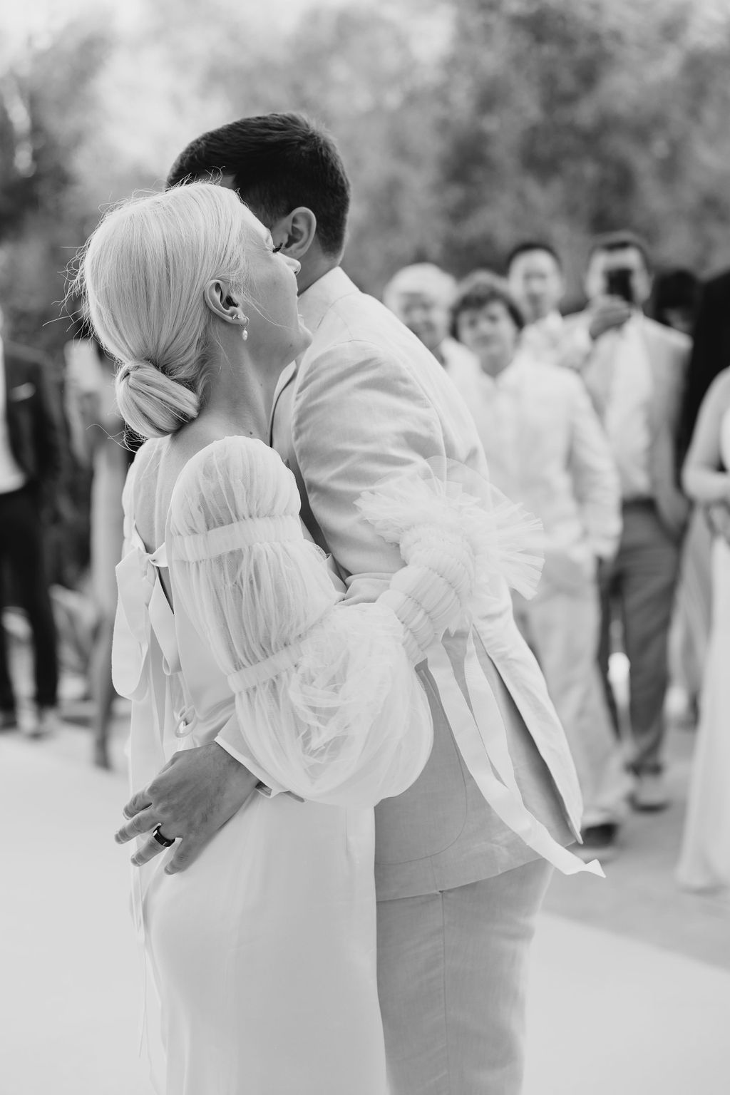 Black and white photo captures an emotional wedding dance moment with onlookers in background.