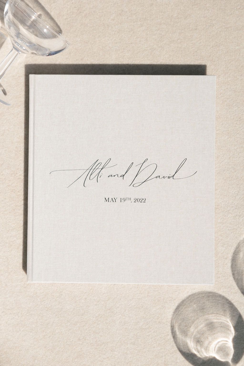 White wedding invitation with elegant calligraphy and date displayed with champagne glasses.