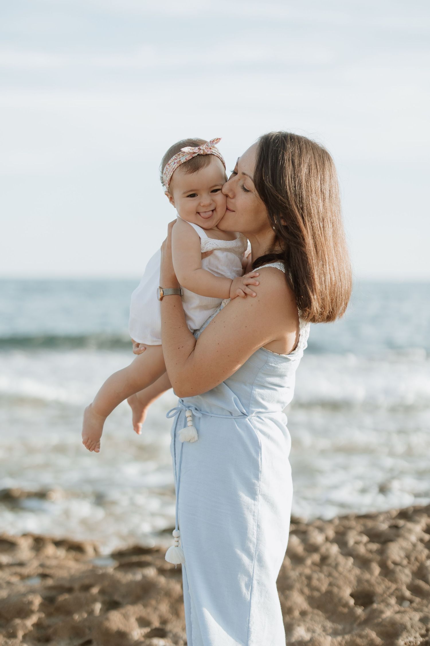 Sweet candid moments captured at a rocky beach shore with light blue clothing.