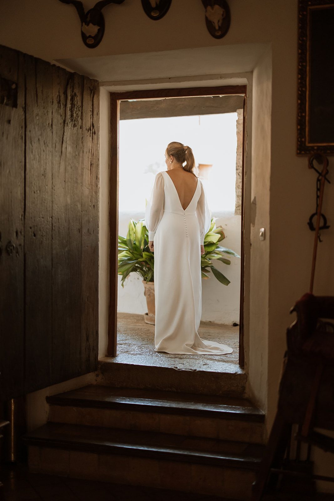 Elegant white wedding dress silhouette framed in rustic wooden doorway.