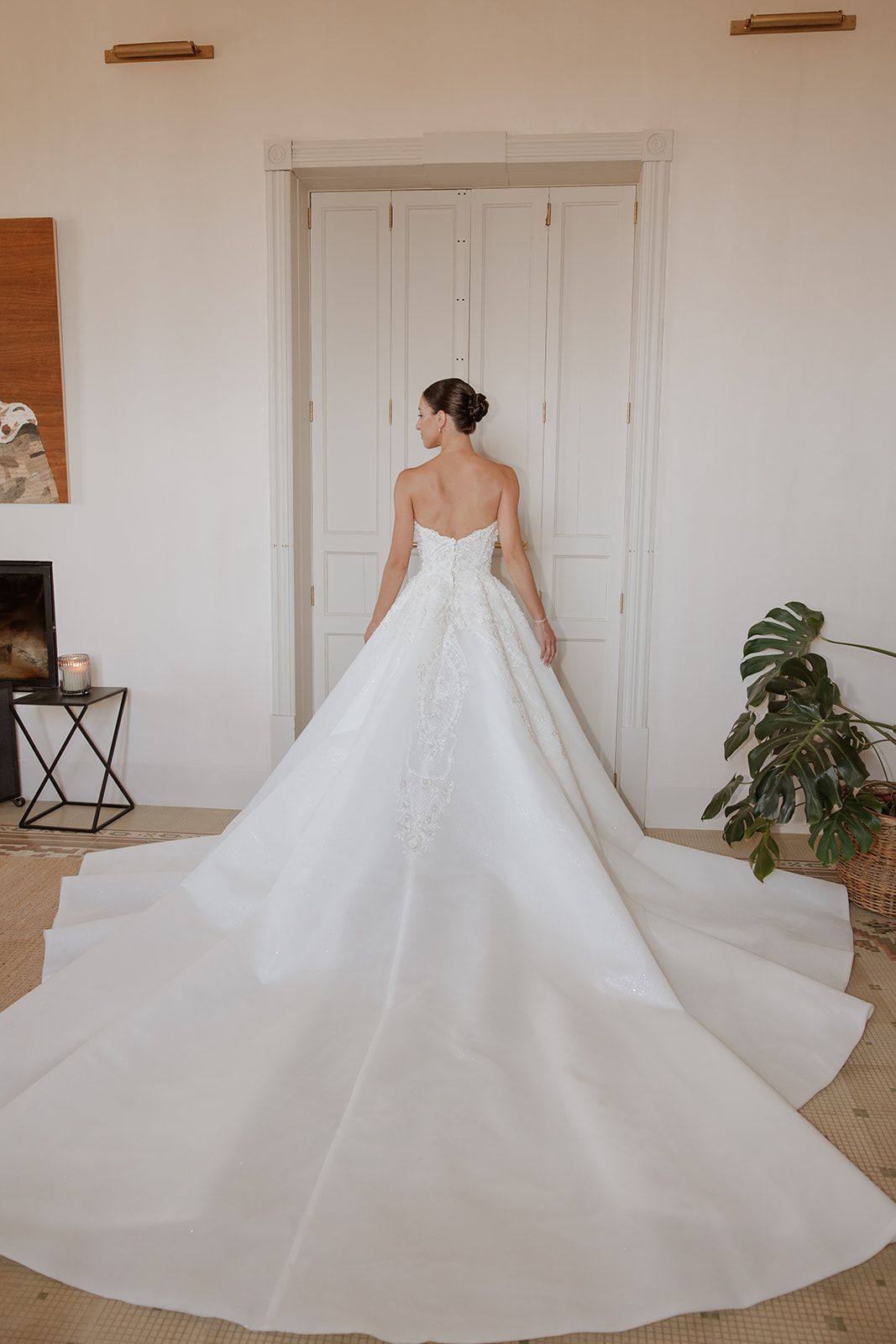 Full-length back view of princess wedding gown with dramatic train in bright room.
