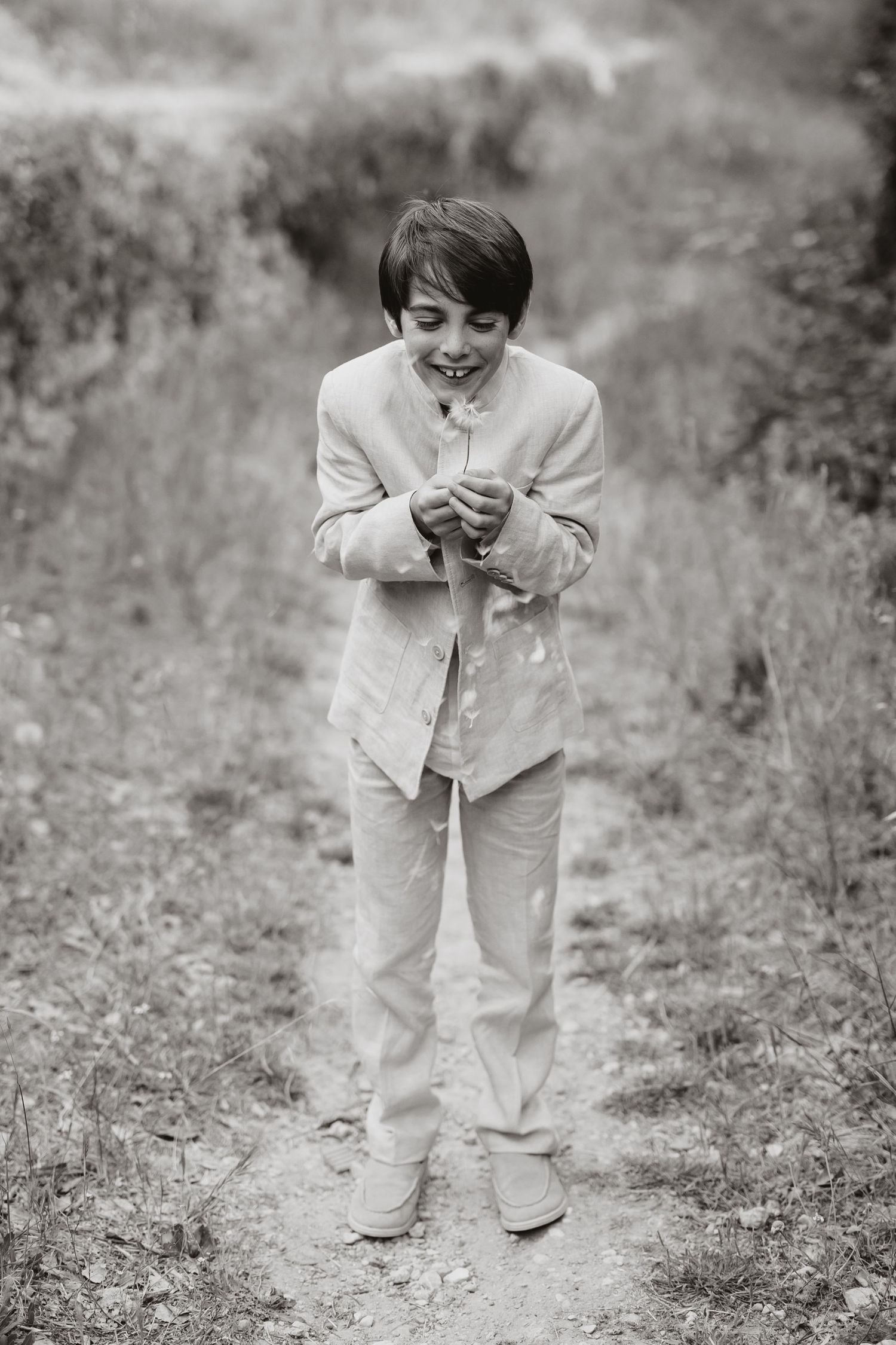 Black and white photo of a young person in light-colored clothing standing on a path and laughing with joy.