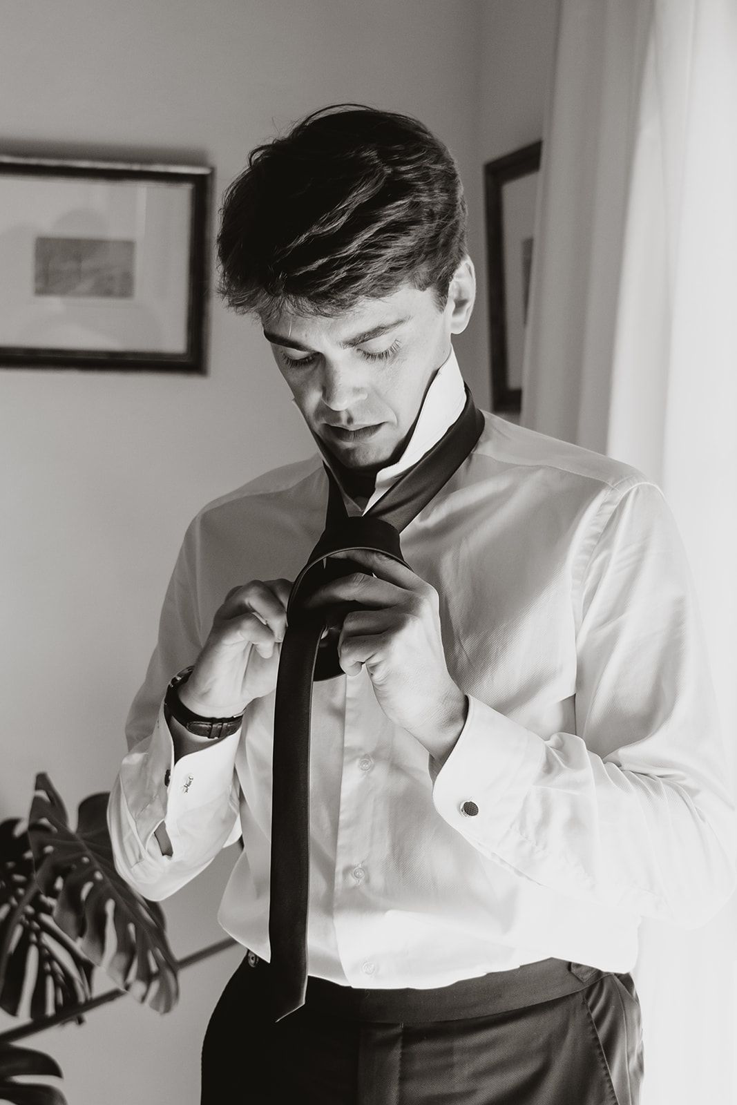 Monochrome image of figure adjusting black tie while wearing white formal shirt.