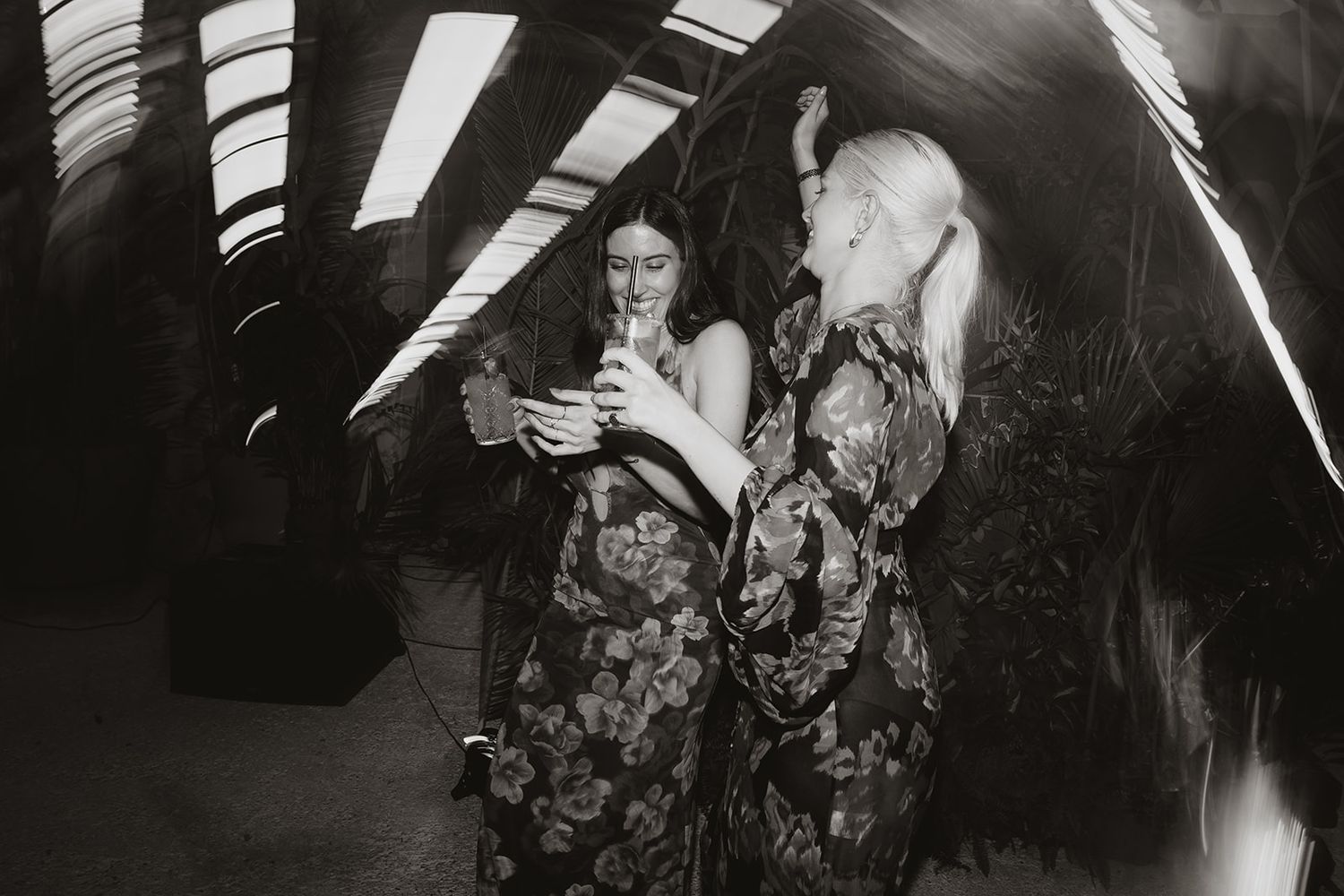 Black and white photo of guests dancing at reception under dramatic lighting.