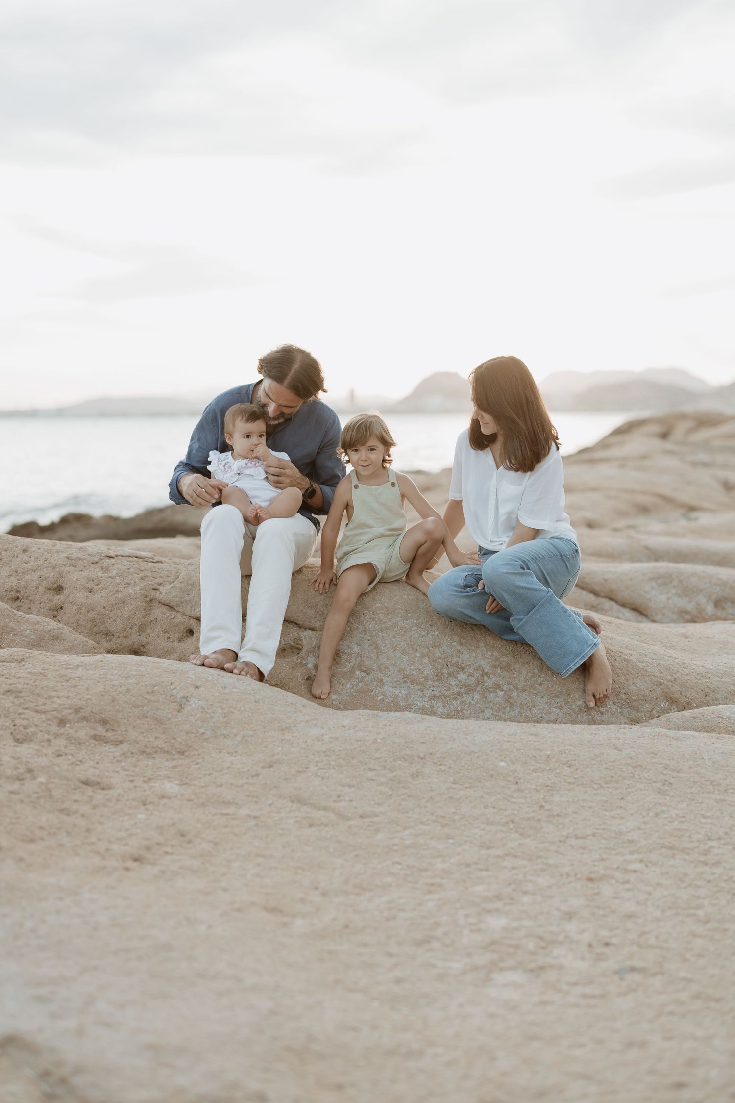 Family relaxing together on large coastal rock formation.