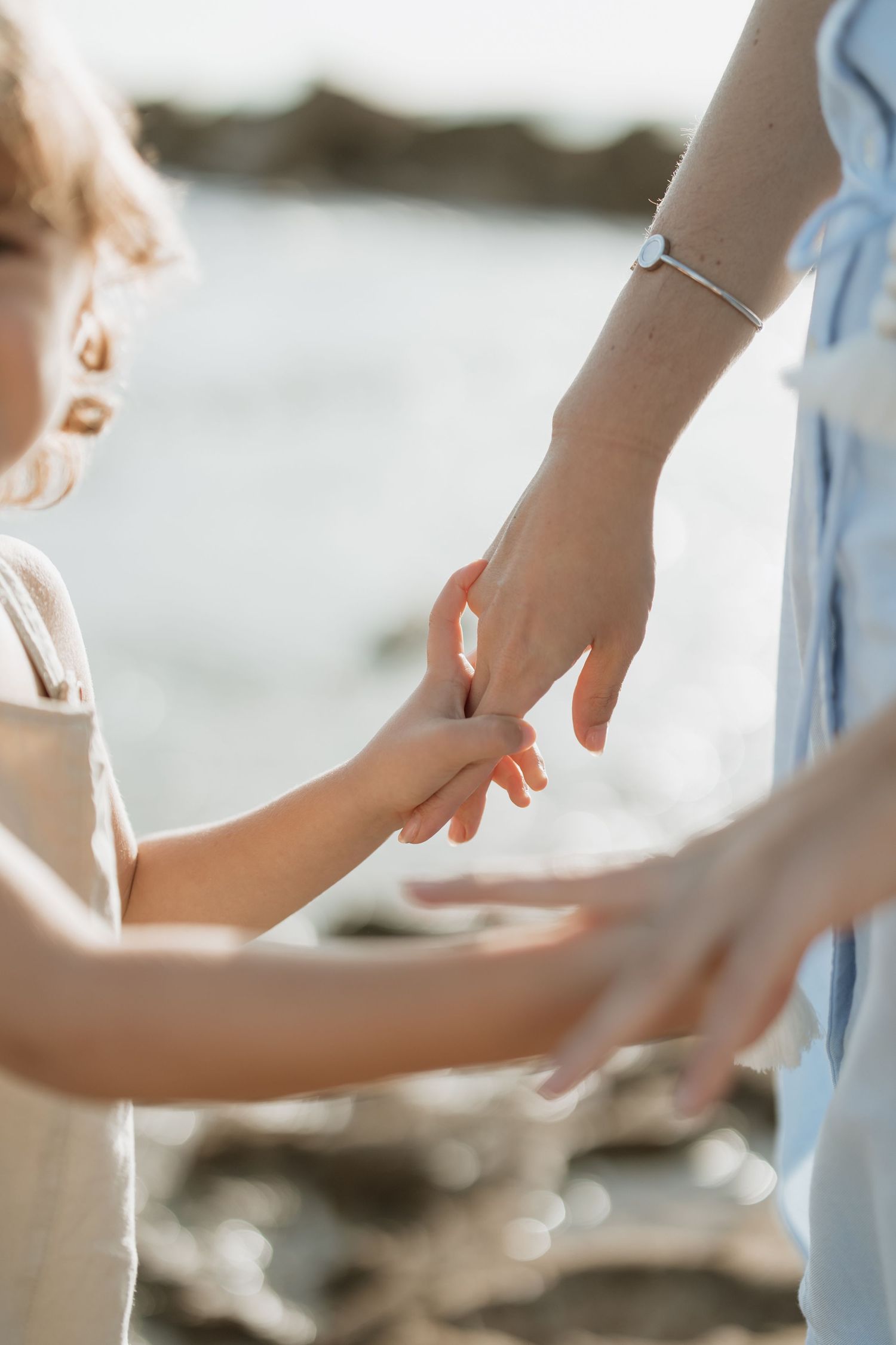 Close up of hands touching tenderly on rocky beach at sunset.