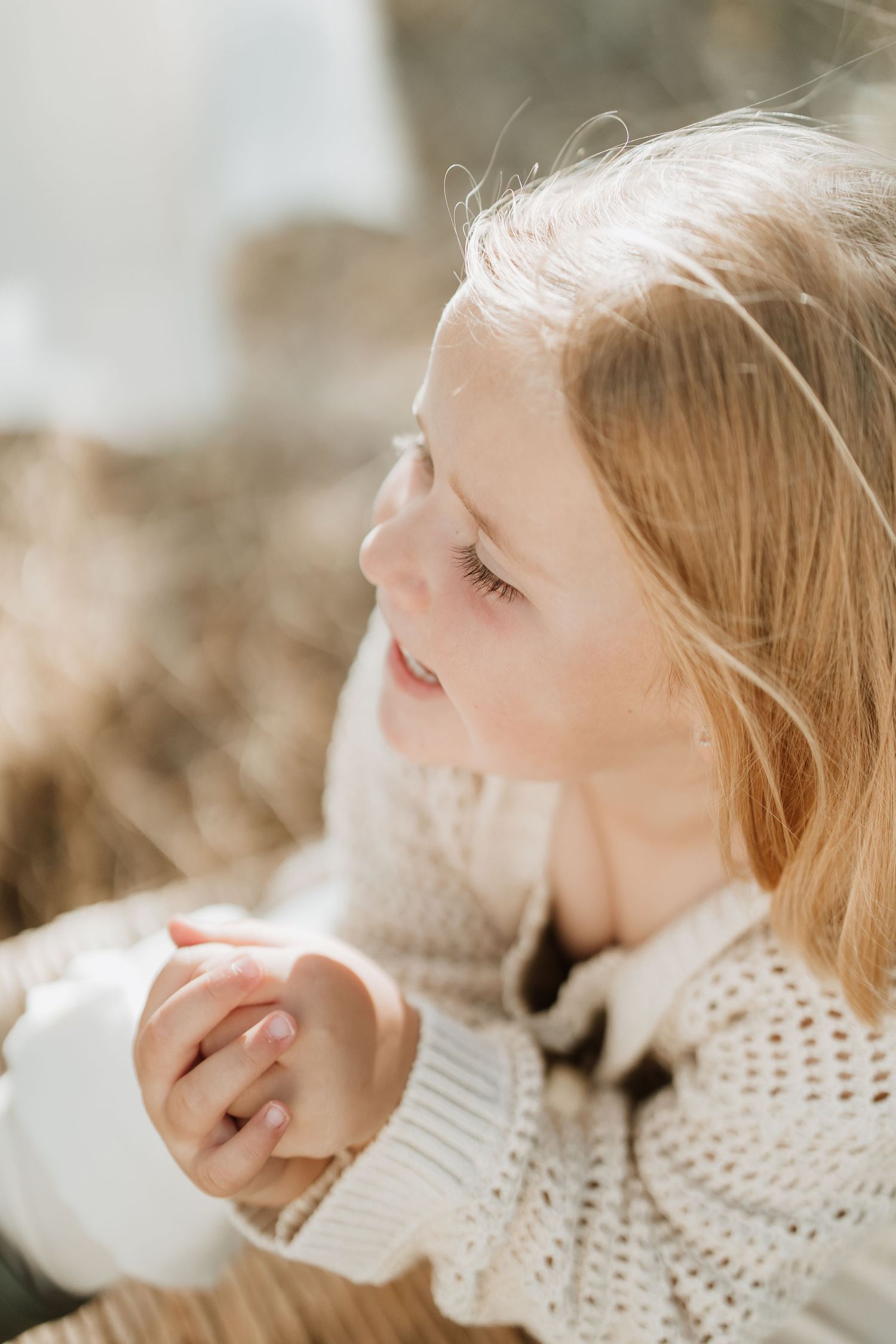 Dreamy profile portrait of child in cream sweater with sunlit hair against natural background.