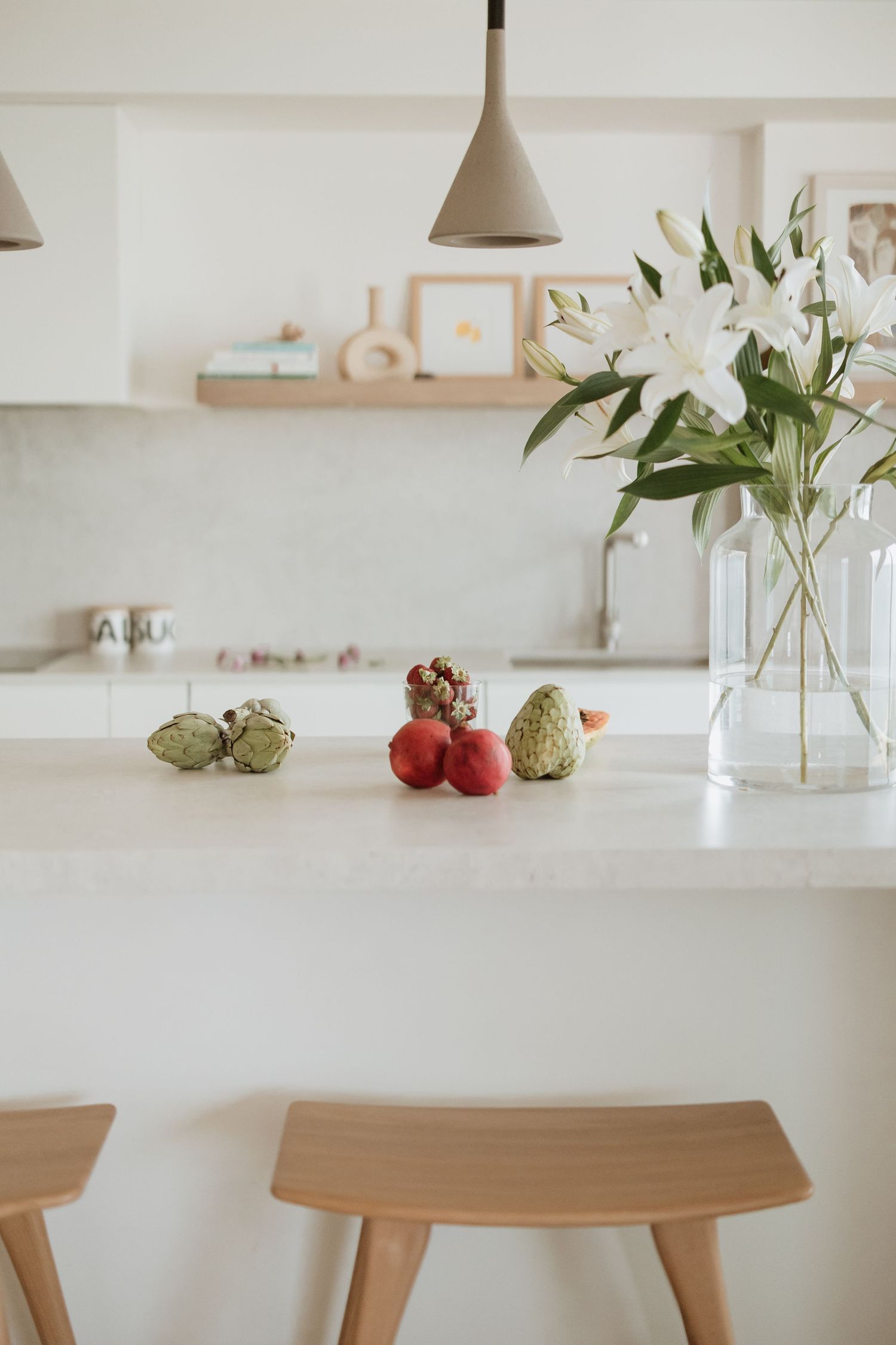 Modern white kitchen counter with fresh lilies and fruit on a minimalist marble surface.
