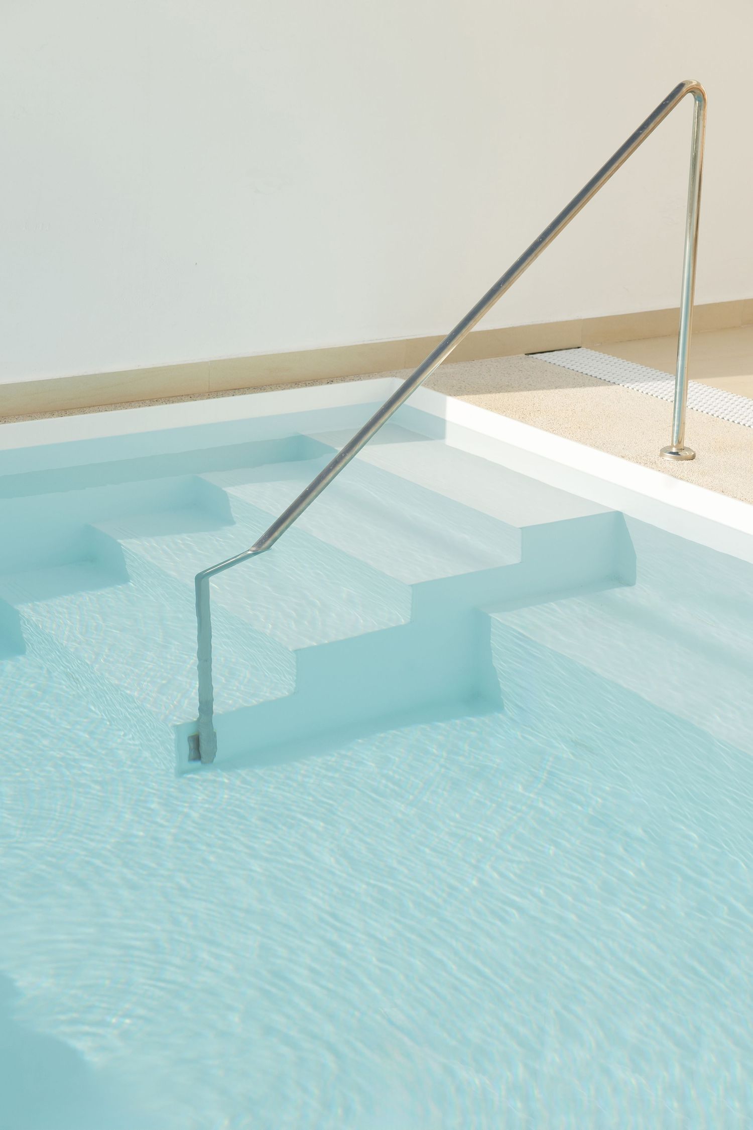 Close-up of pool steps with metal handrail descending into crystal clear turquoise water.