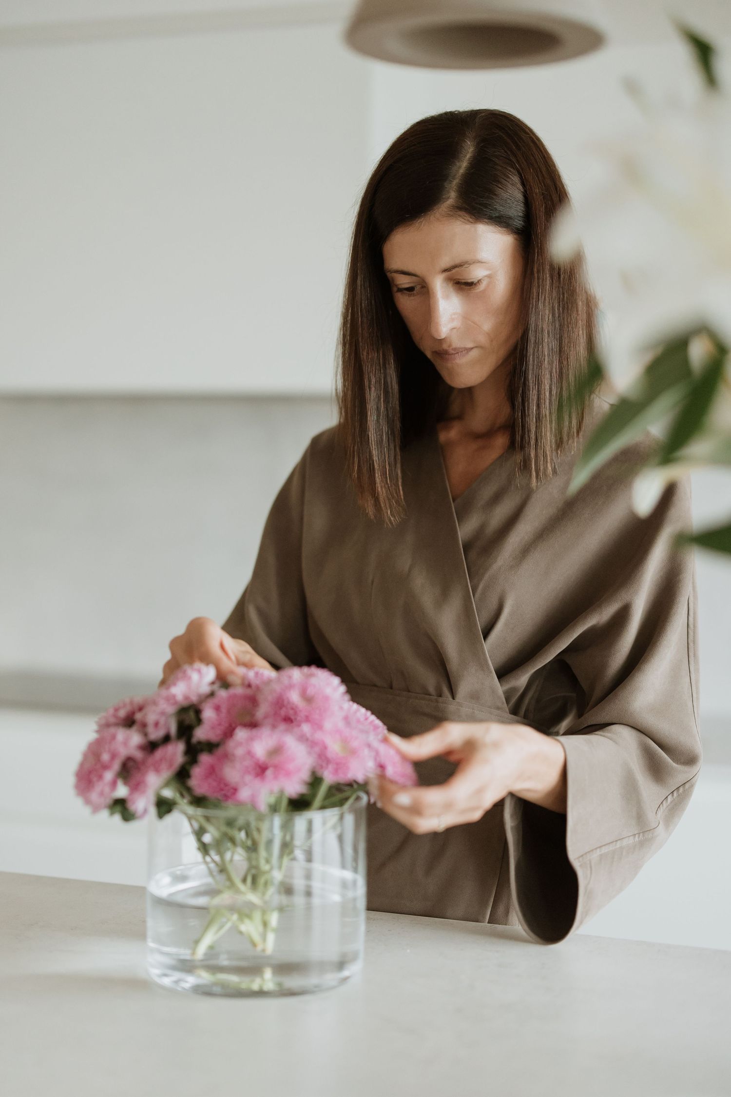 Person in brown sweater arranging pink flowers in glass vase.