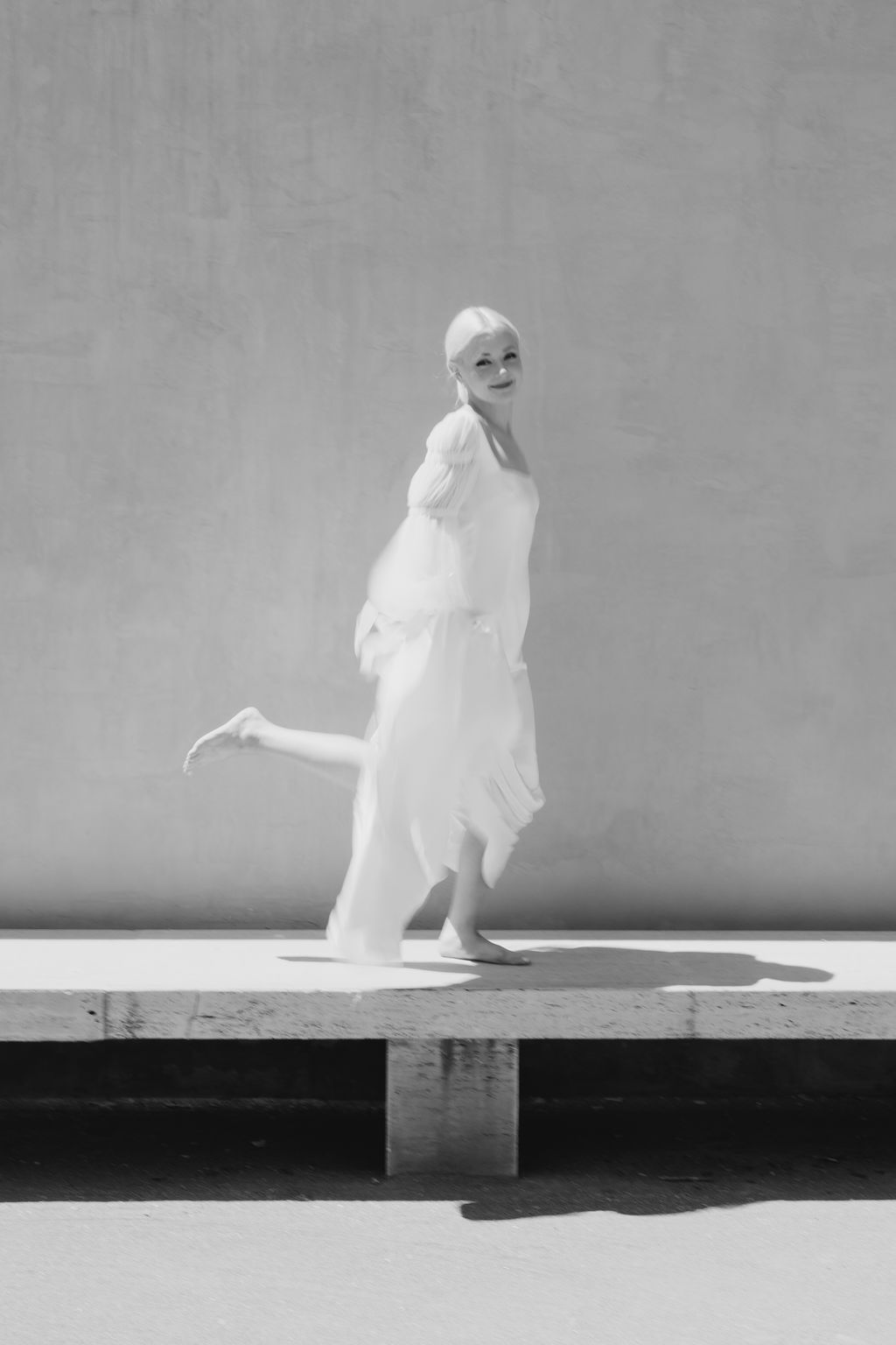 Artistic monochrome portrait of a figure in white dress against a minimalist backdrop.