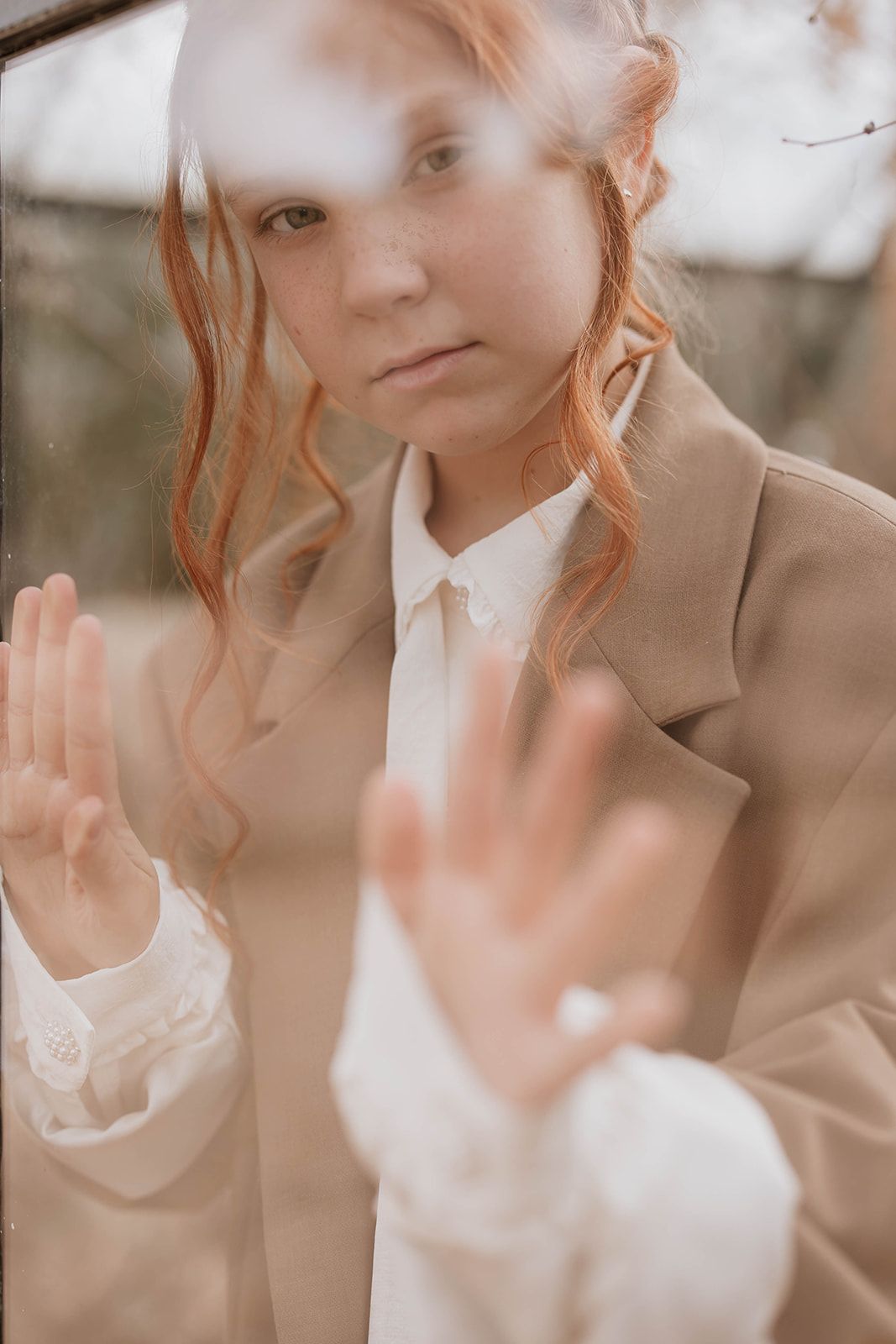Soft-focus portrait showing hands pressed against glass with a brown coat in warm tones.