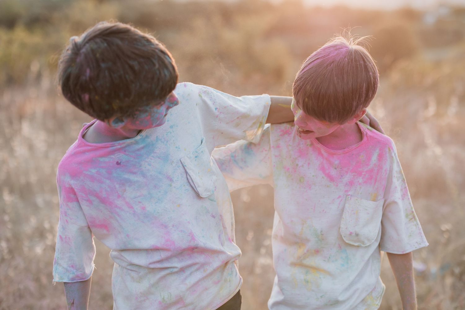 Two people wearing white clothes playing with colorful pink powder during outdoor Holi festival celebrations.