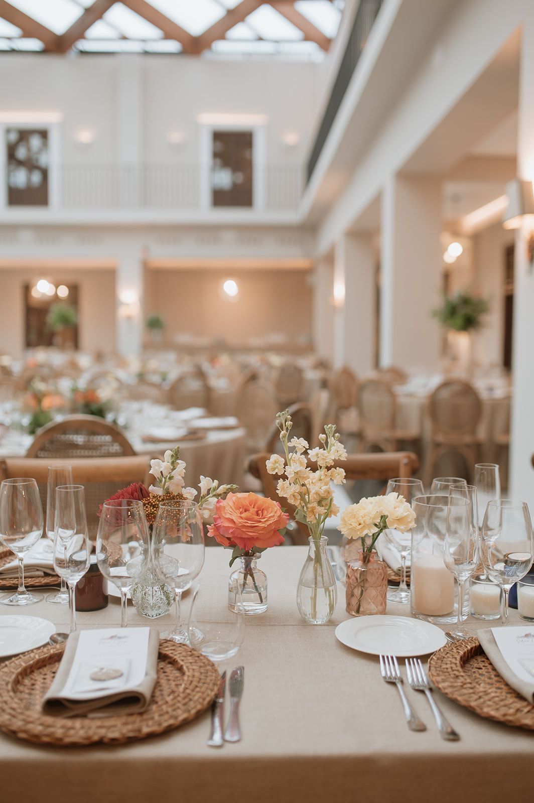 Wedding table settings with woven placemats, wine glasses, and delicate floral centerpieces.