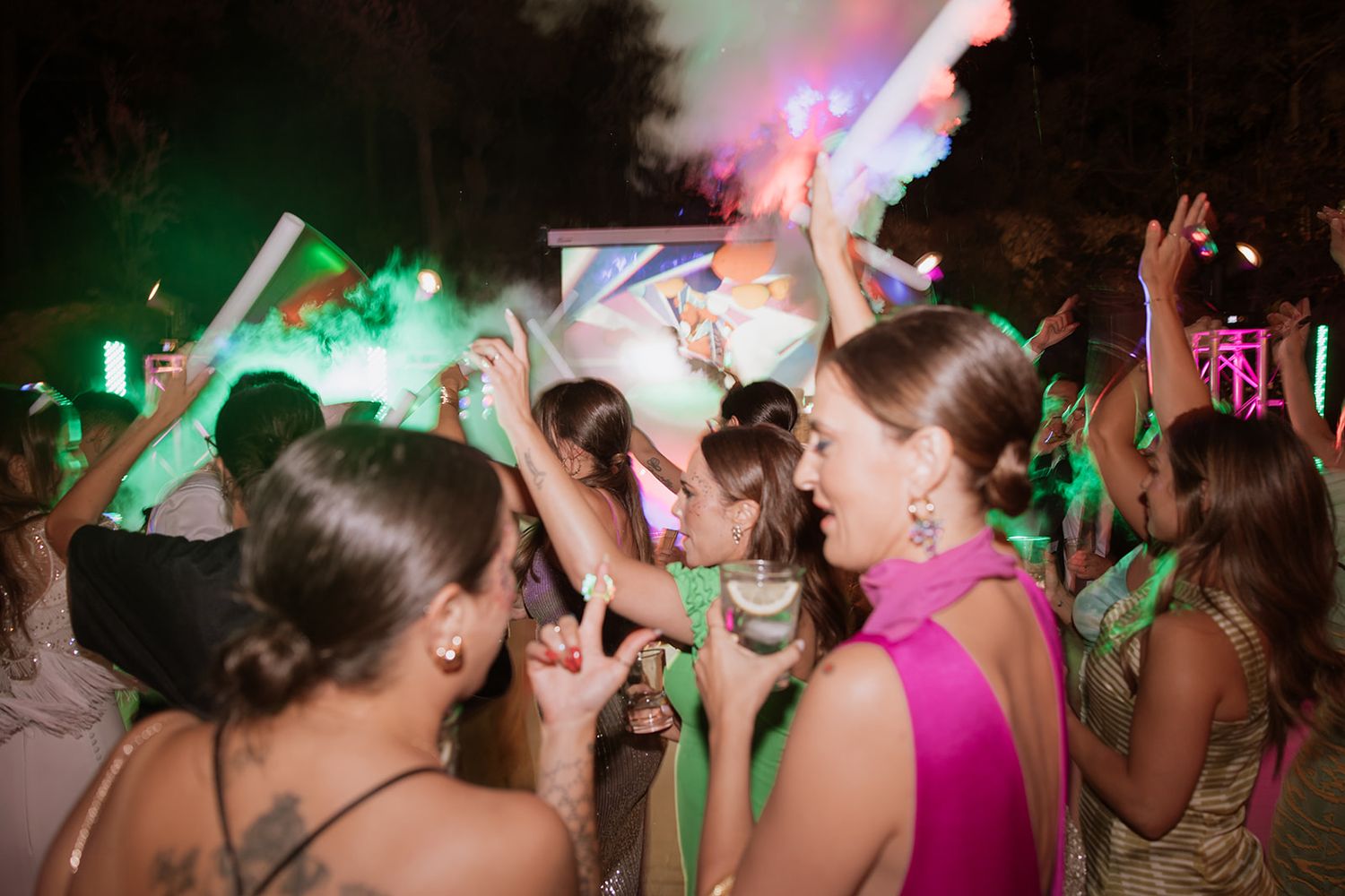 Crowd dancing under colorful lights at an outdoor nighttime party.