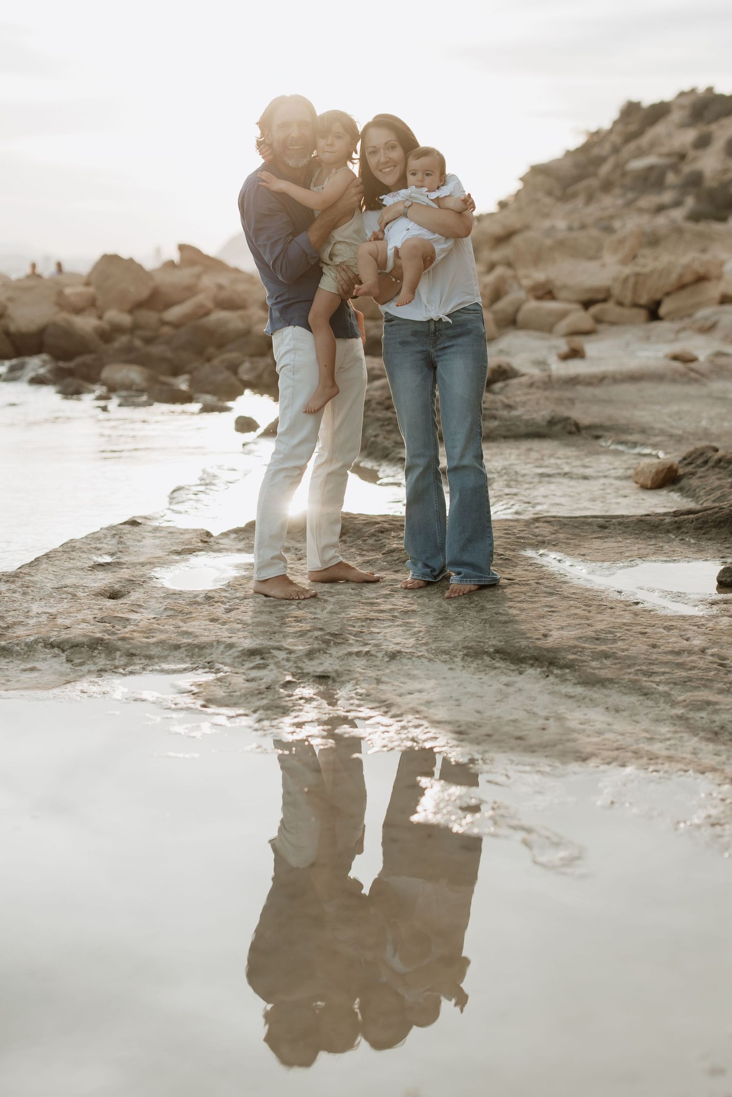 Family moment captured at rocky beach with reflection in still water.