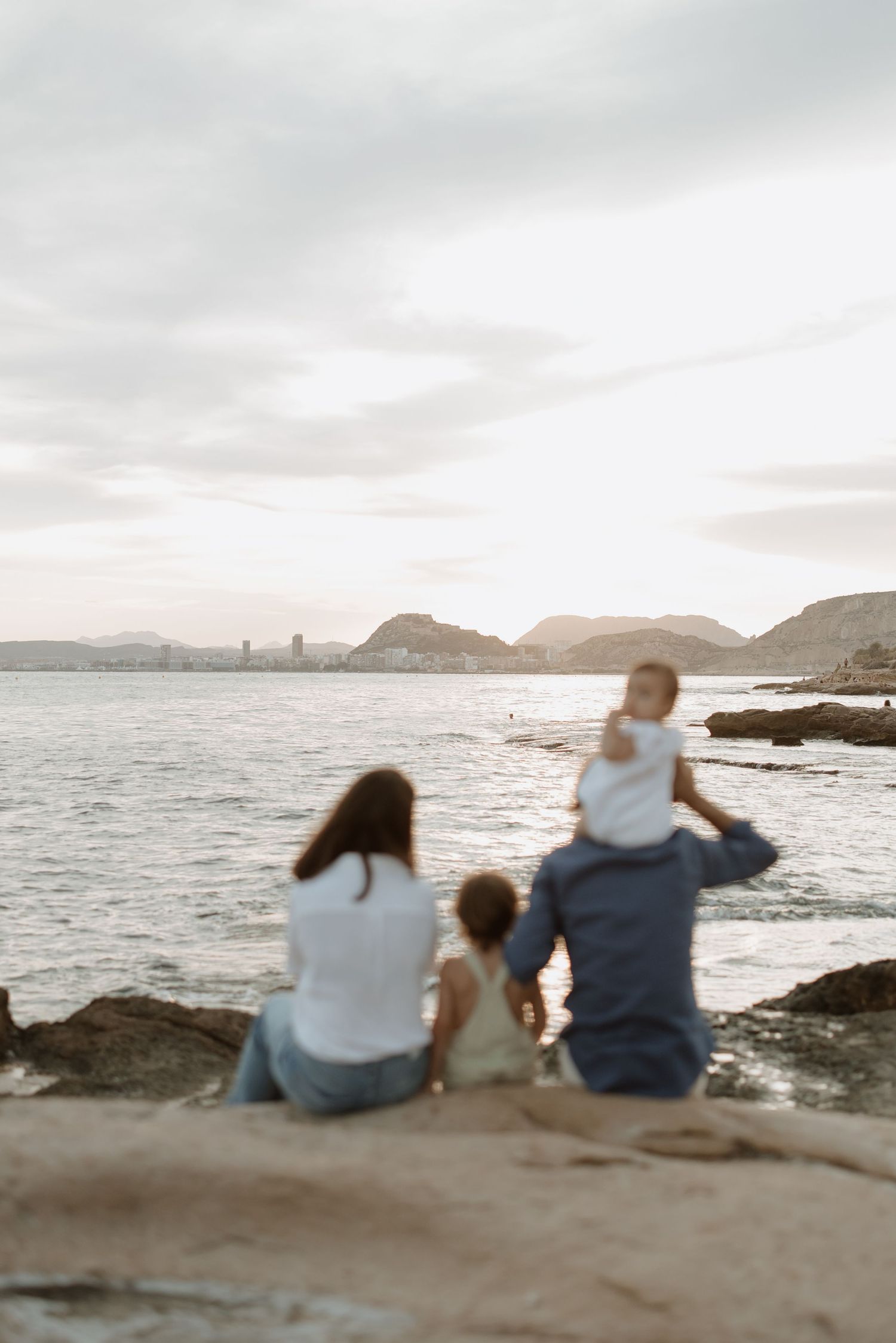Family enjoying sunset view together while seated on coastal rocks.
