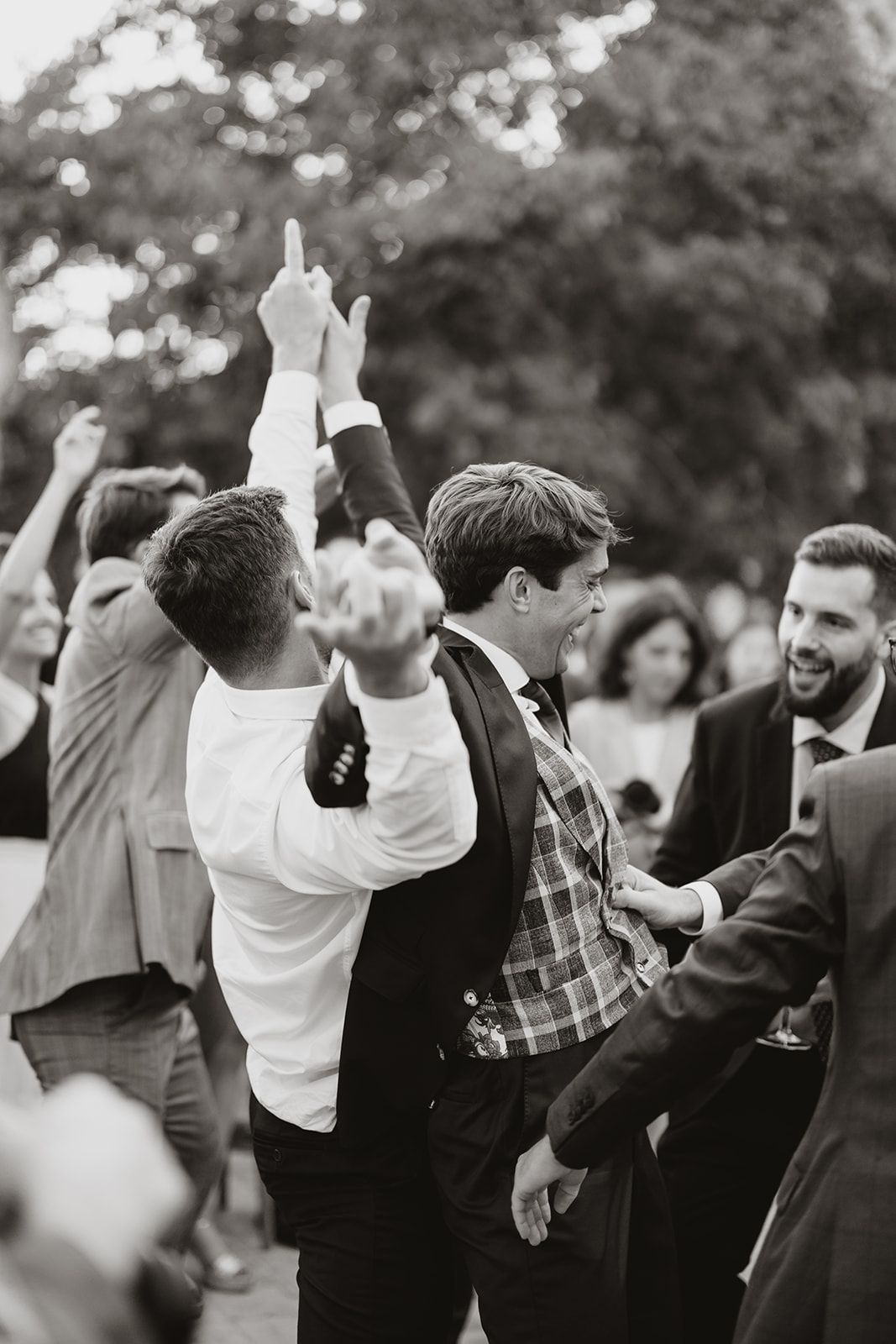 Wedding guests dance energetically with raised hands at an outdoor celebration.