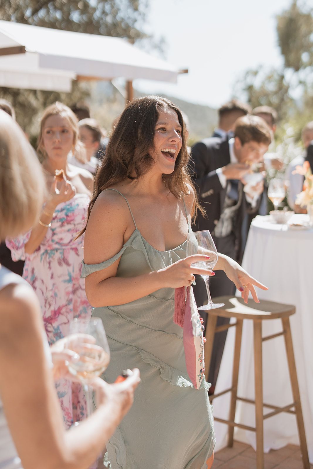Woman in sage green dress laughs joyfully during outdoor wedding celebration.