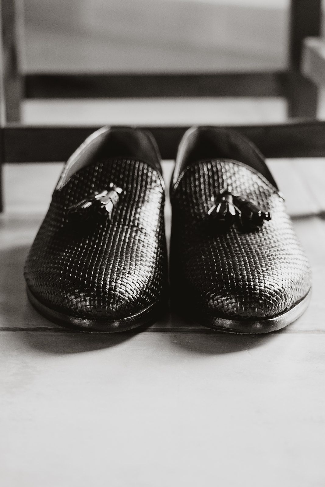 Close-up of textured black formal dress shoes on light floor.